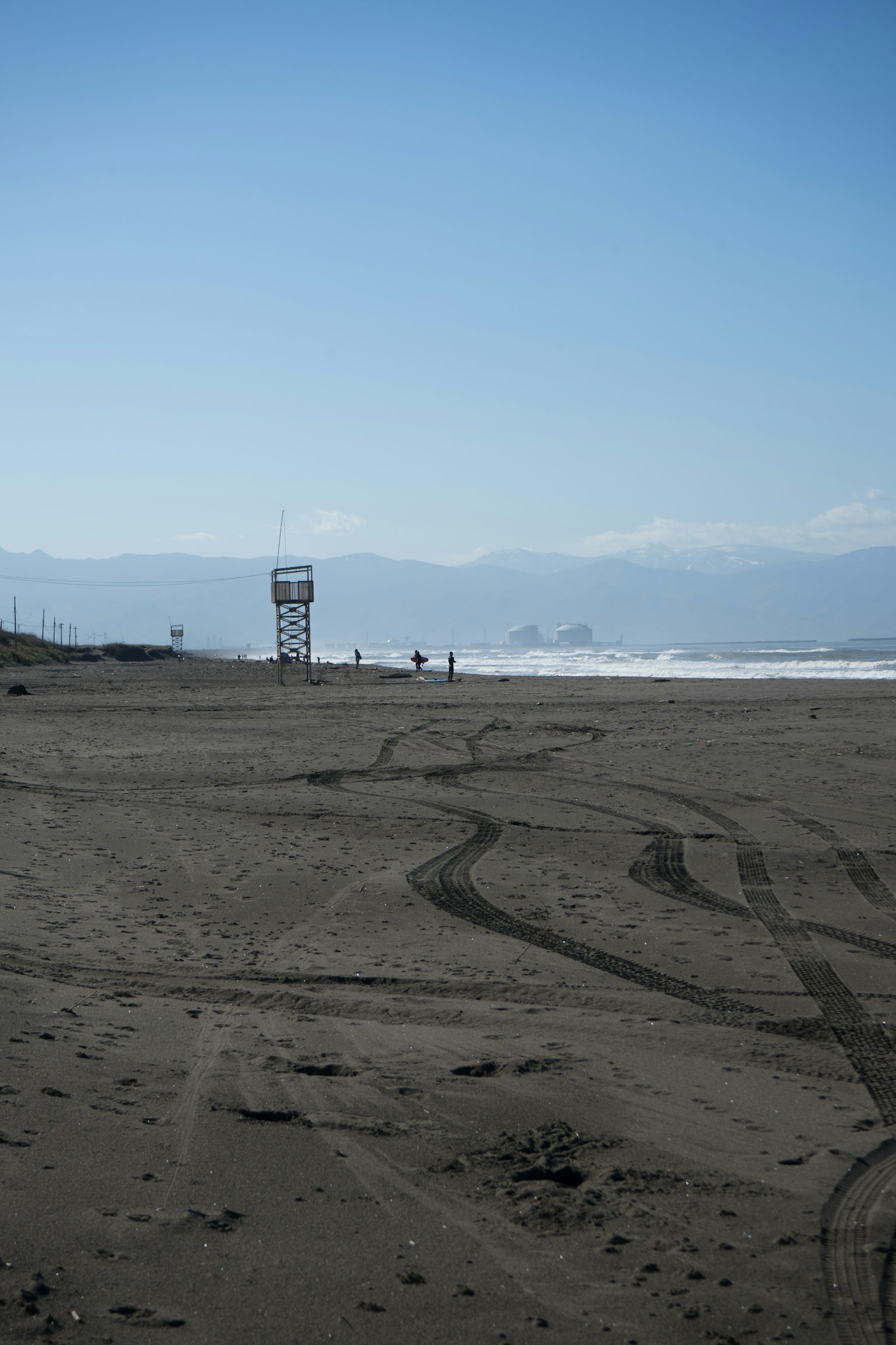 Scena costiera con una torre di salvataggio e spiaggia sabbiosa sotto un cielo blu e montagne lontane