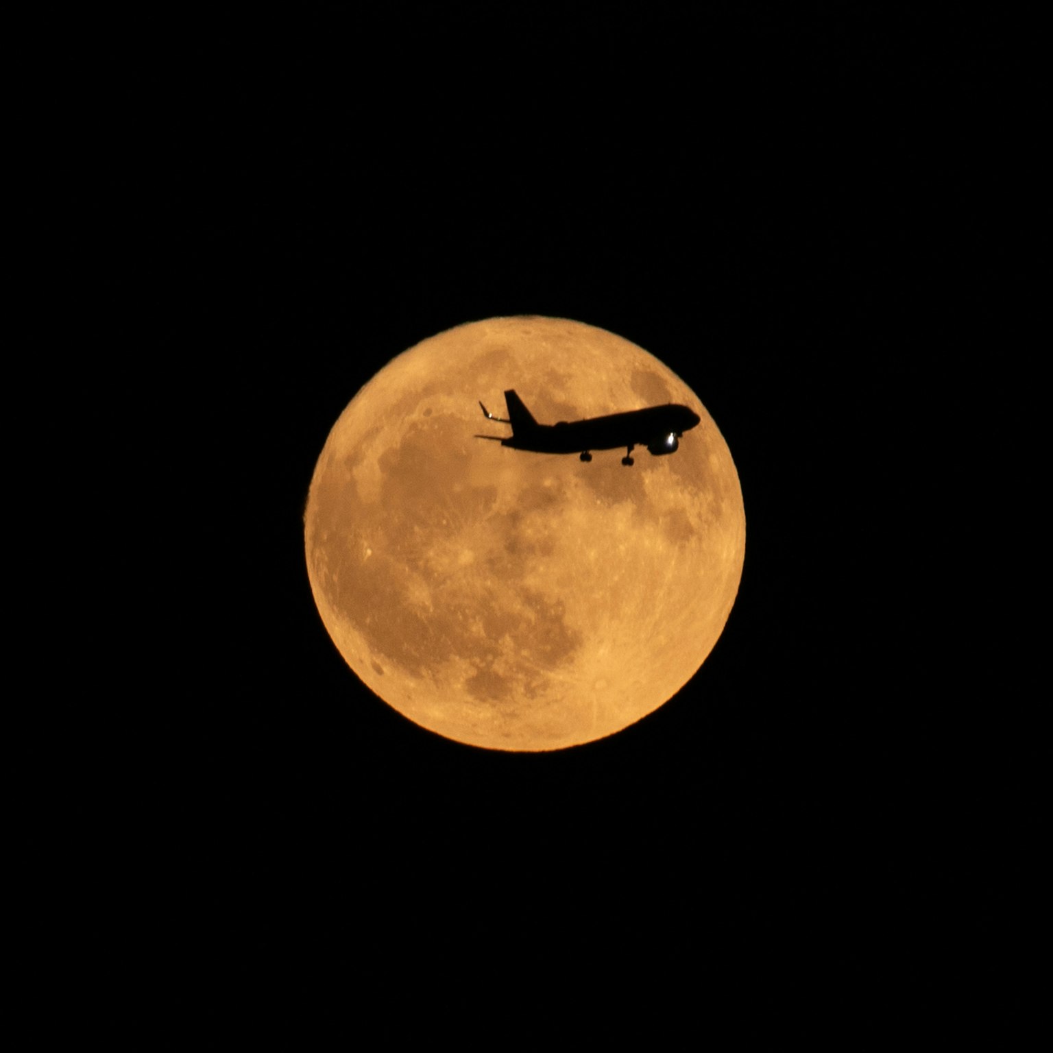 Siluet pesawat terbang di depan bulan purnama oranye