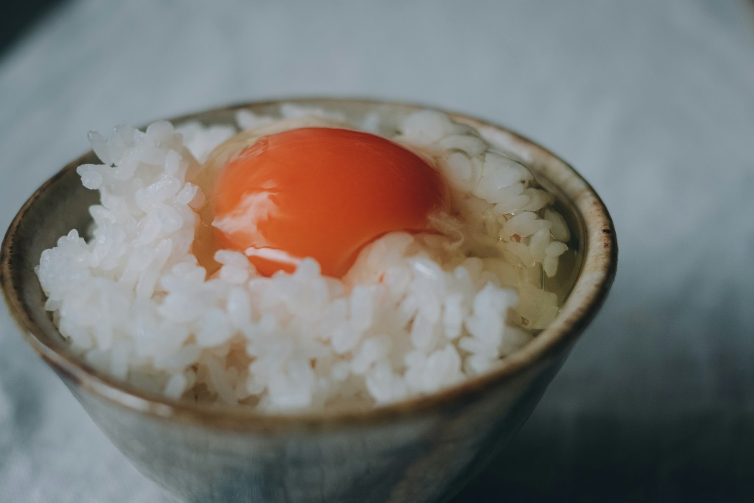 Eine Keramikschale mit weißem Reis, gekrönt von einem leuchtend orangefarbenen Eigelb