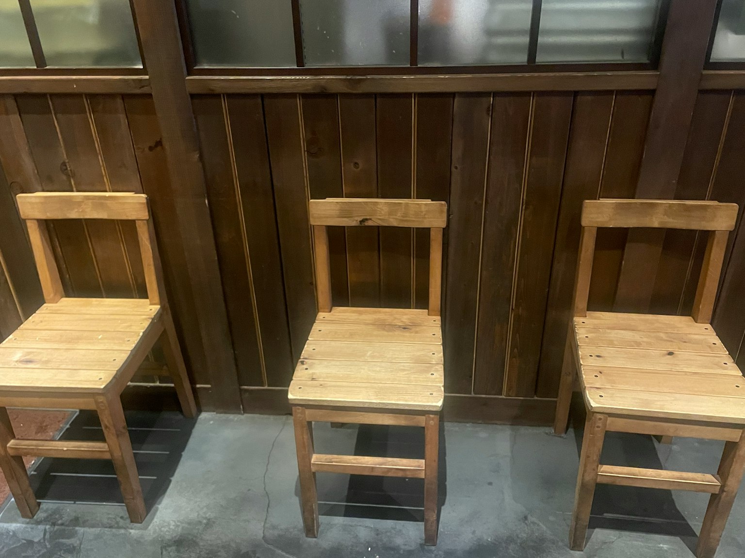 Three wooden chairs arranged against a wooden wall