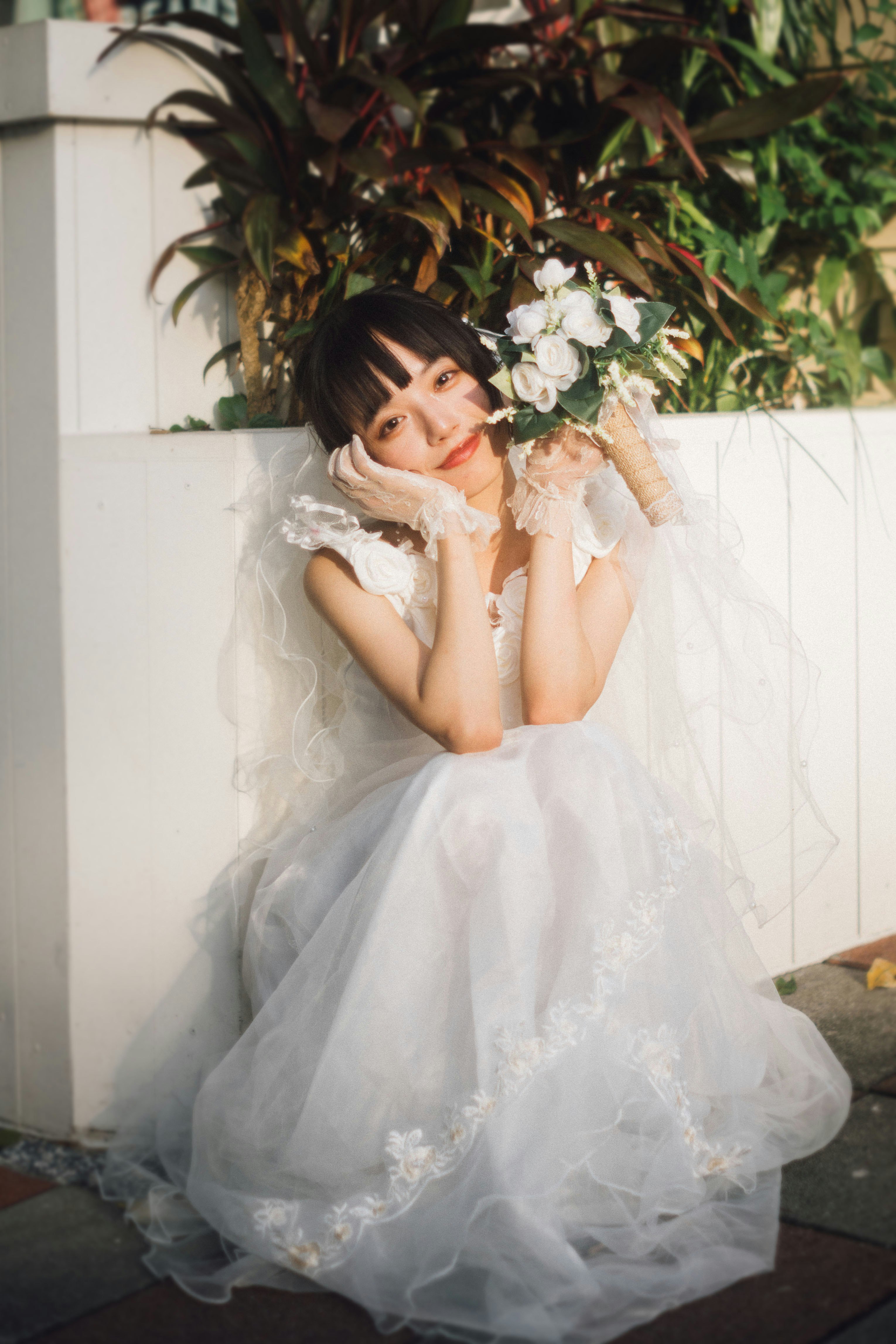 花と白い壁の前で微笑むふんわりドレスの女性
