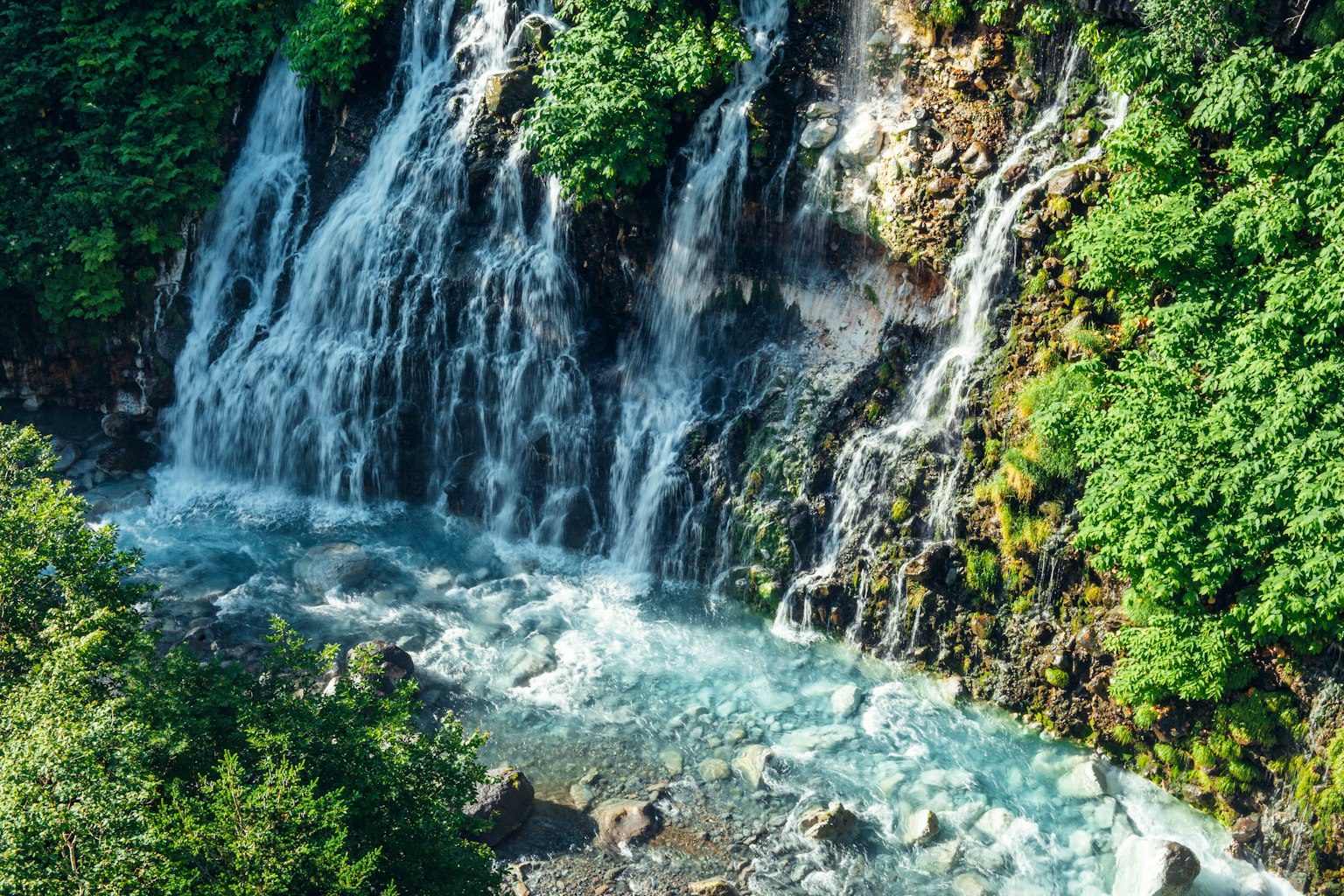 Belle cascade entourée d'arbres verts luxuriants avec de l'eau bleue claire