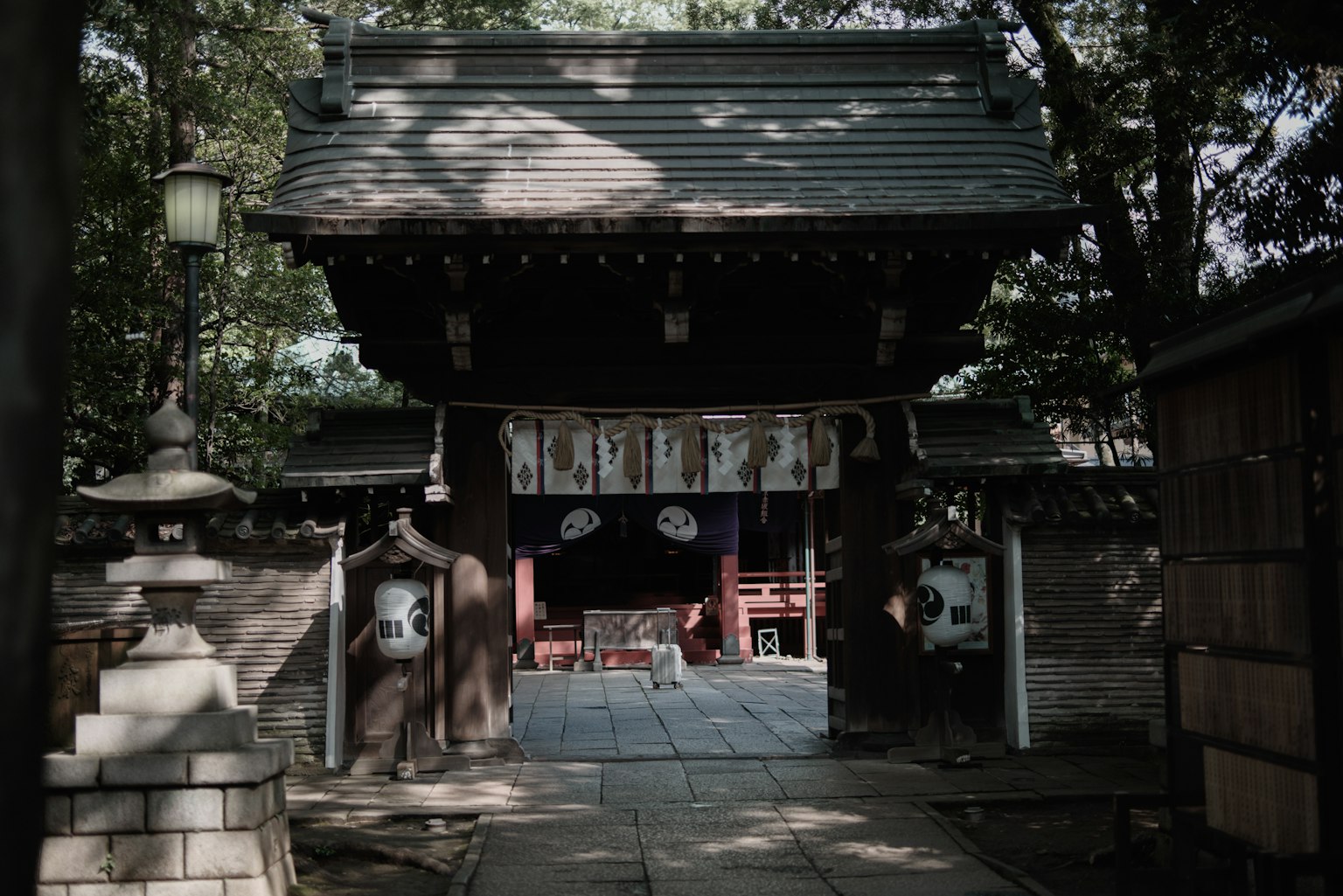 An old shrine gate surrounded by trees with traditional lanterns