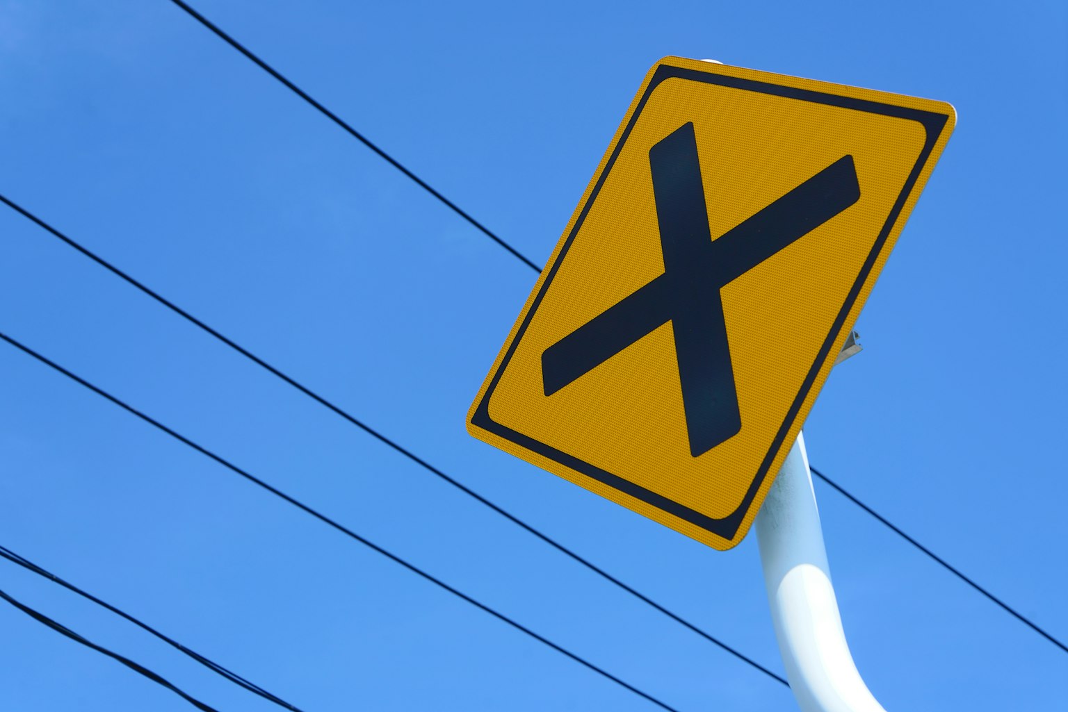 Panneau d'intersection jaune avec un marque X noir sur fond de ciel bleu