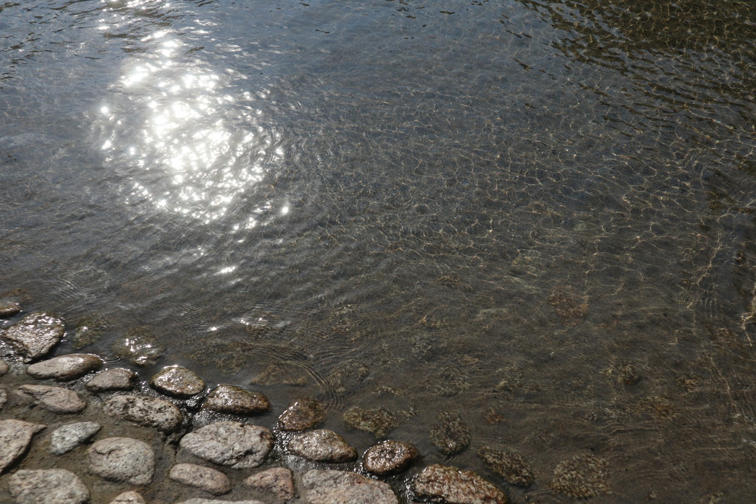 A tranquil river scene featuring sunlight reflections on the water and a stone border