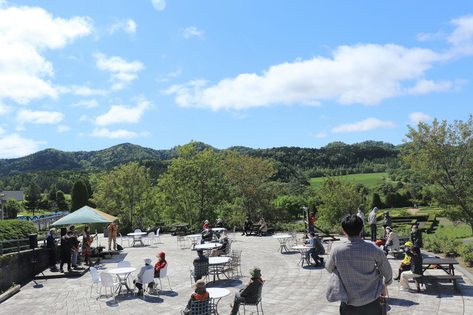 Terraza de café al aire libre con personas disfrutando bajo un cielo azul montañas verdes al fondo