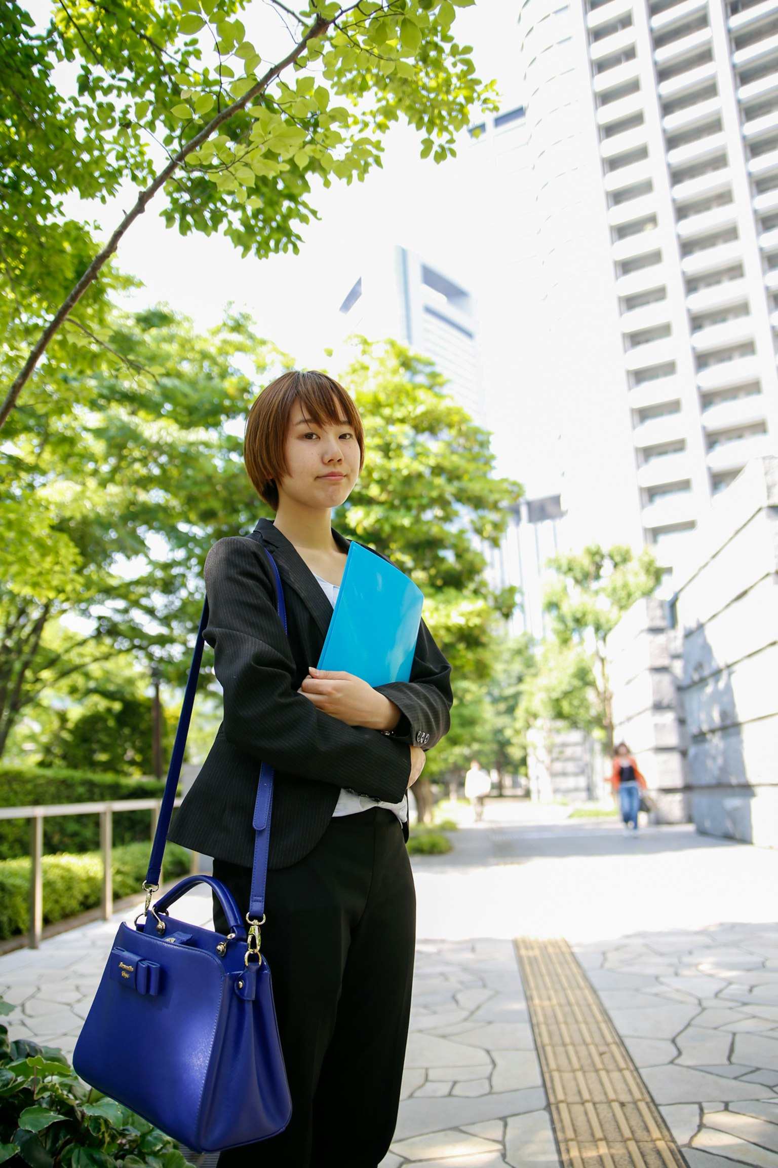 一位穿着商务套装的女性在城市公园里手持蓝色文件夹和蓝色包包