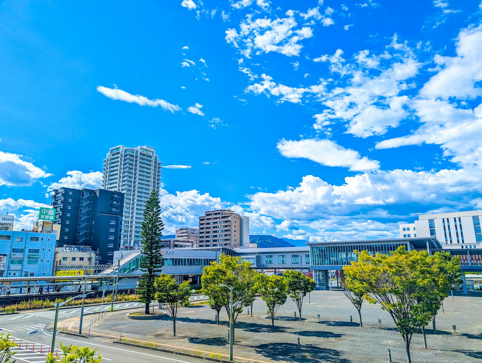 Paysage urbain avec ciel bleu et nuages présentant des bâtiments hauts et des arbres verts