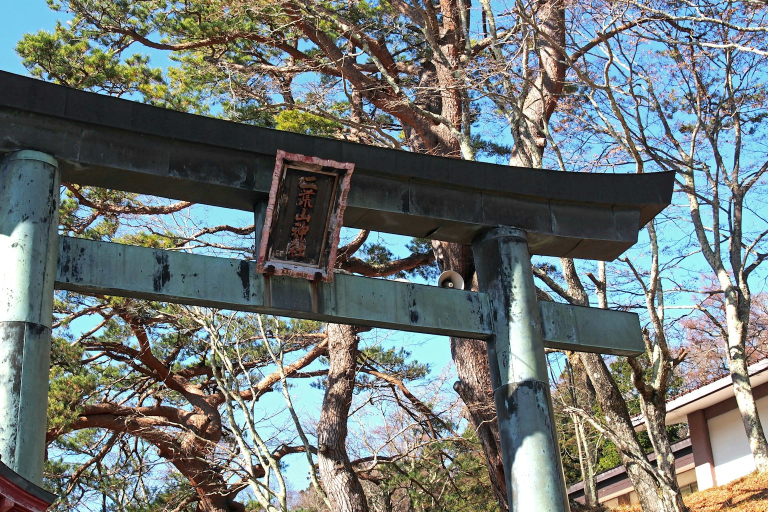 Gerbang torii tua di bawah langit biru dengan pohon-pohon di sekitarnya