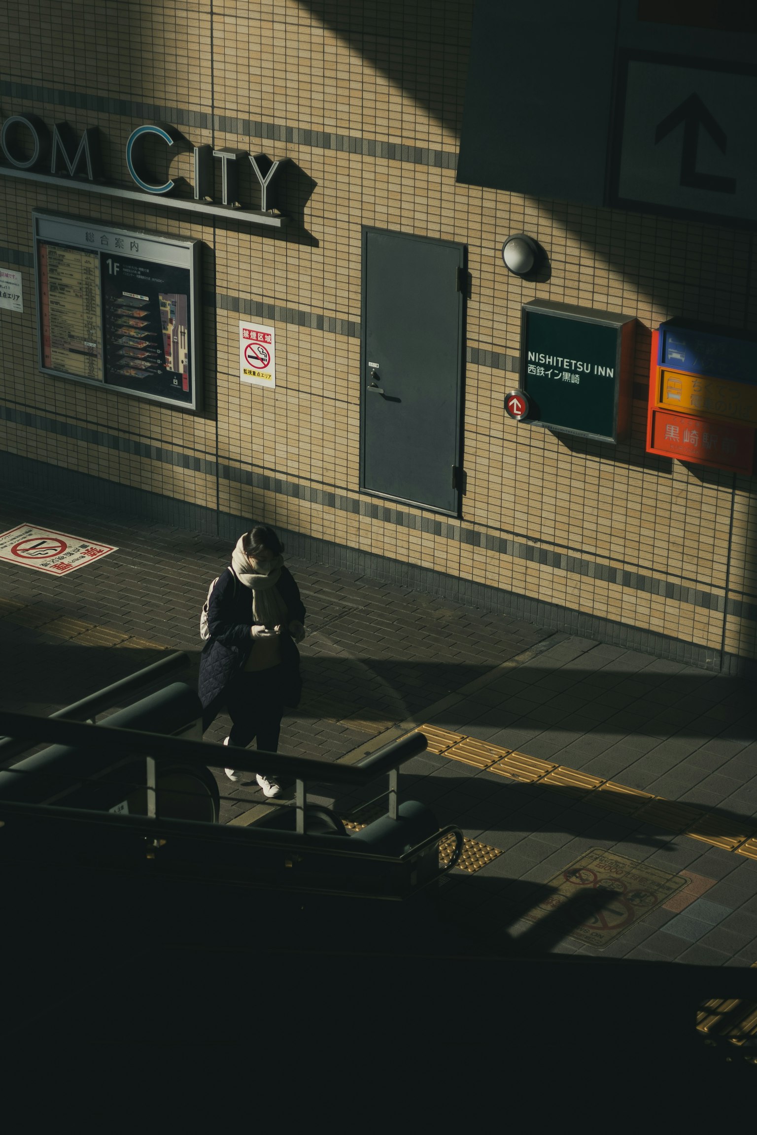 Una persona in attesa su una banchina della stazione con contrasti di luce e ombra