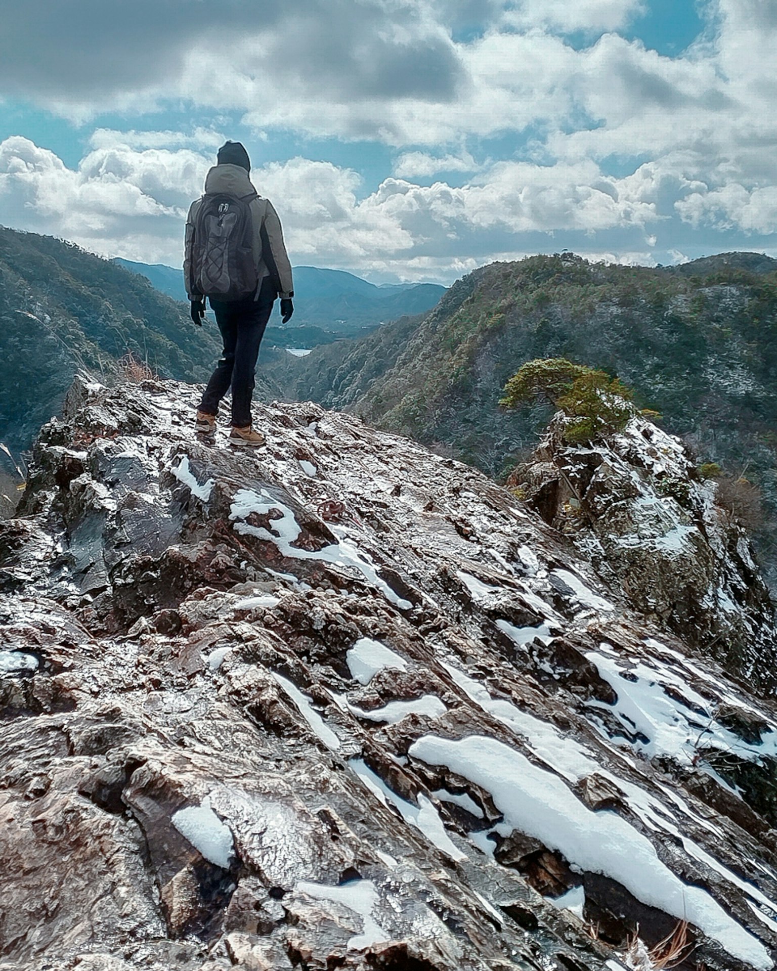 Hiker walking on rocky terrain with snow and mountains in the background