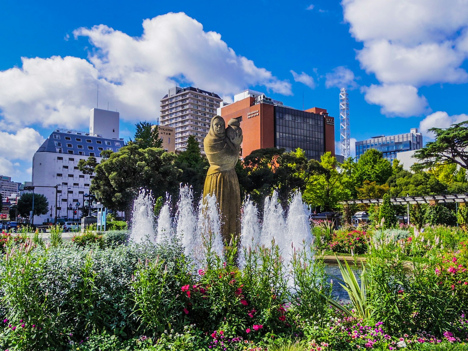 公園的風景，有噴泉和五彩繽紛的花朵，背景是摩天大樓