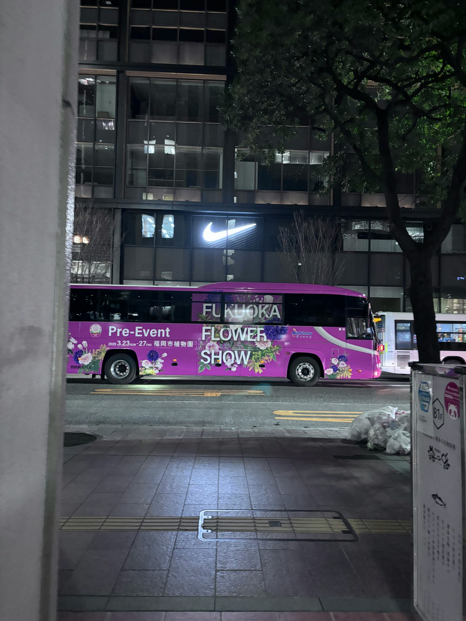Un autobús rosa que anuncia un espectáculo de flores estacionado en una calle de la ciudad por la noche