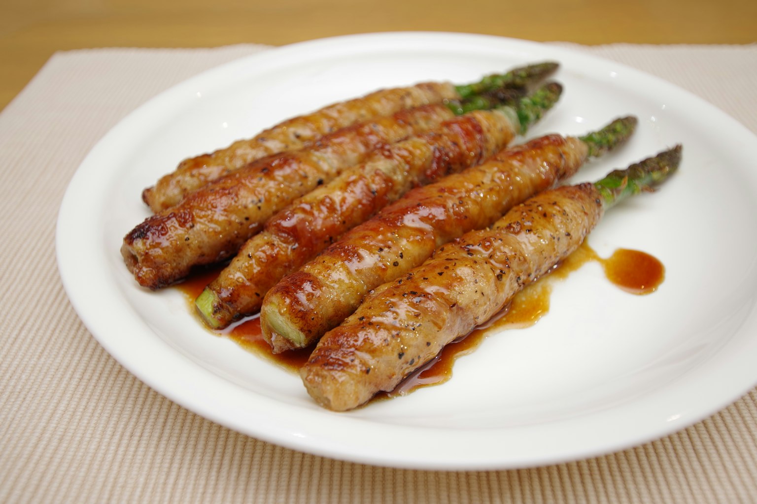 Ein Teller mit in Fleisch gewickelten Spargelspitzen mit Sauce