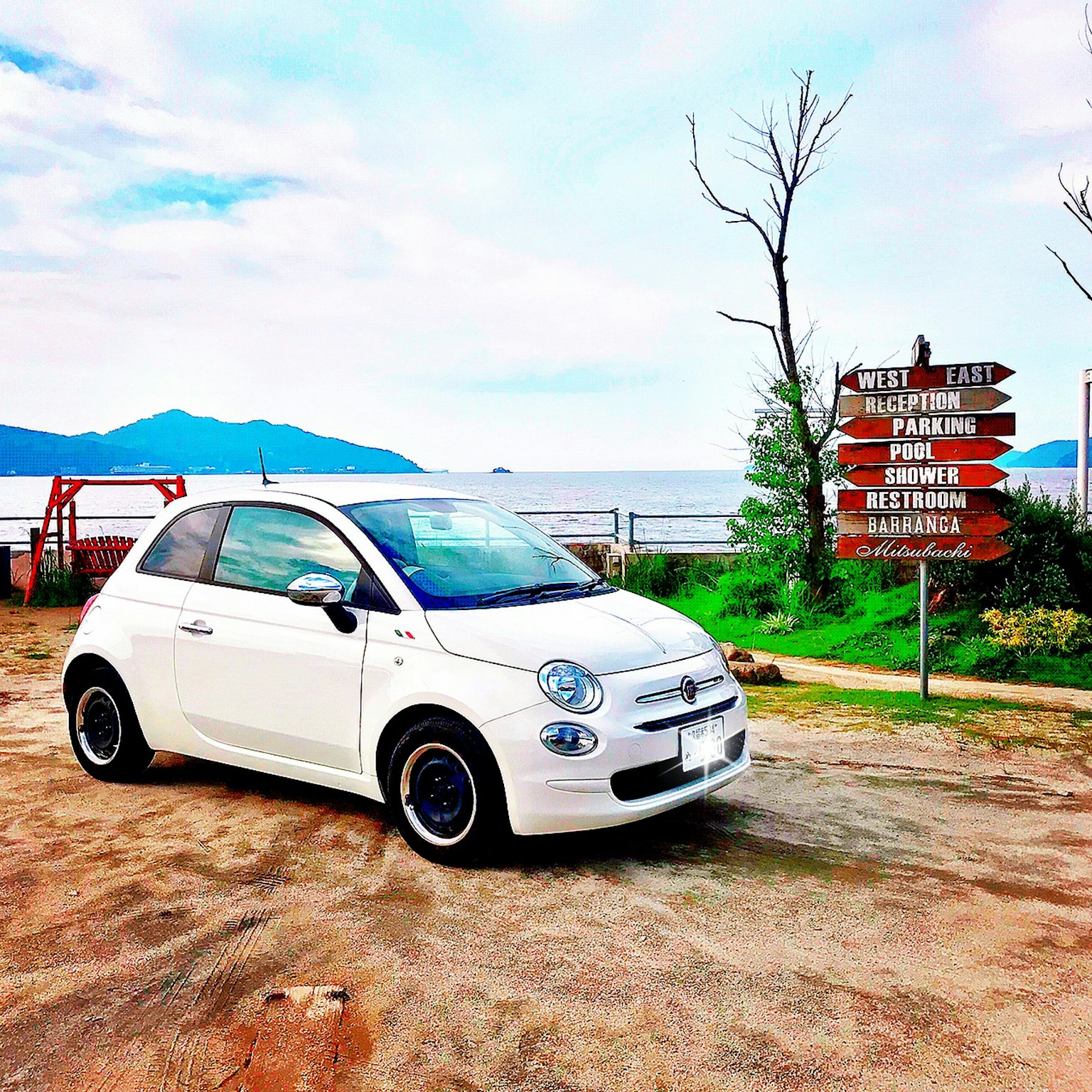 Một chiếc Fiat 500 màu trắng đậu gần biển với biển chỉ dẫn