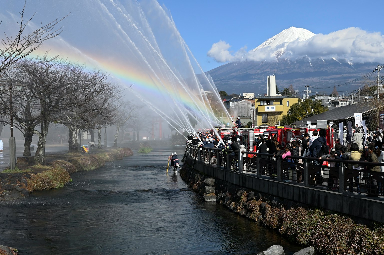 Malersiche Aussicht auf einen Fluss mit Wasserstrahlen, die einen Regenbogen unter dem Fuji bilden