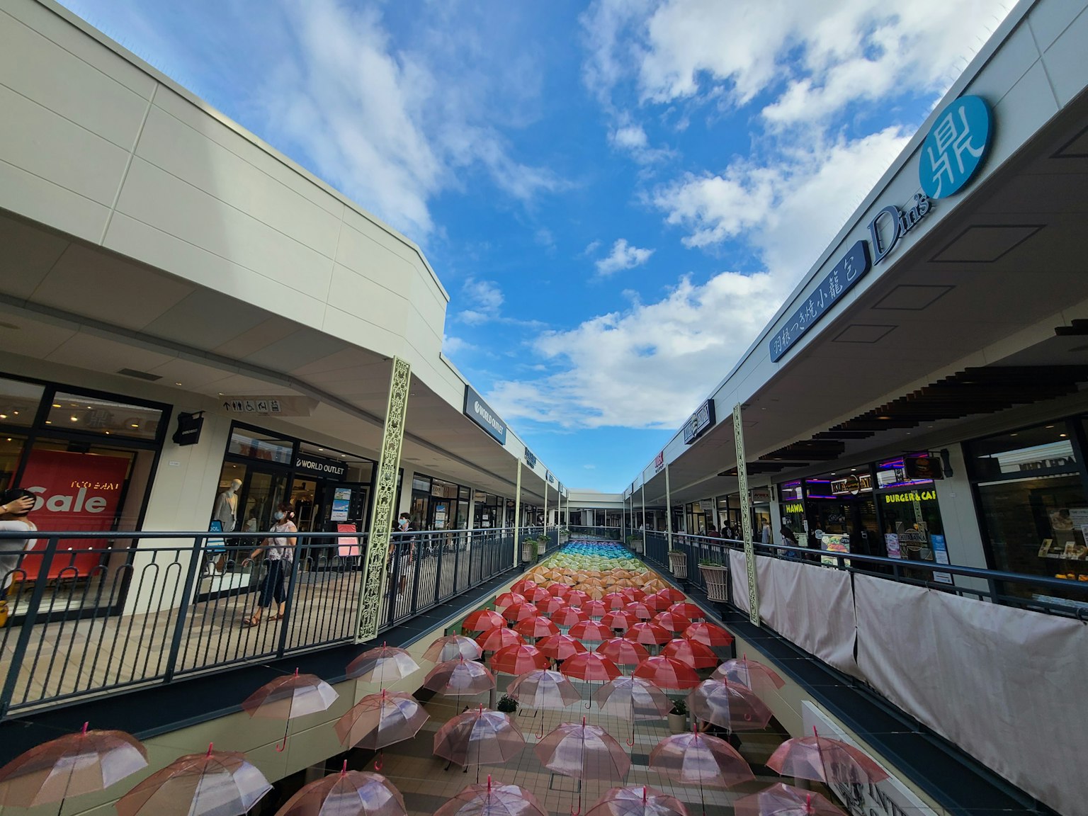 Einkaufszentrum Gehweg unter blauem Himmel mit roter Regenschirm-Kunstinstallation