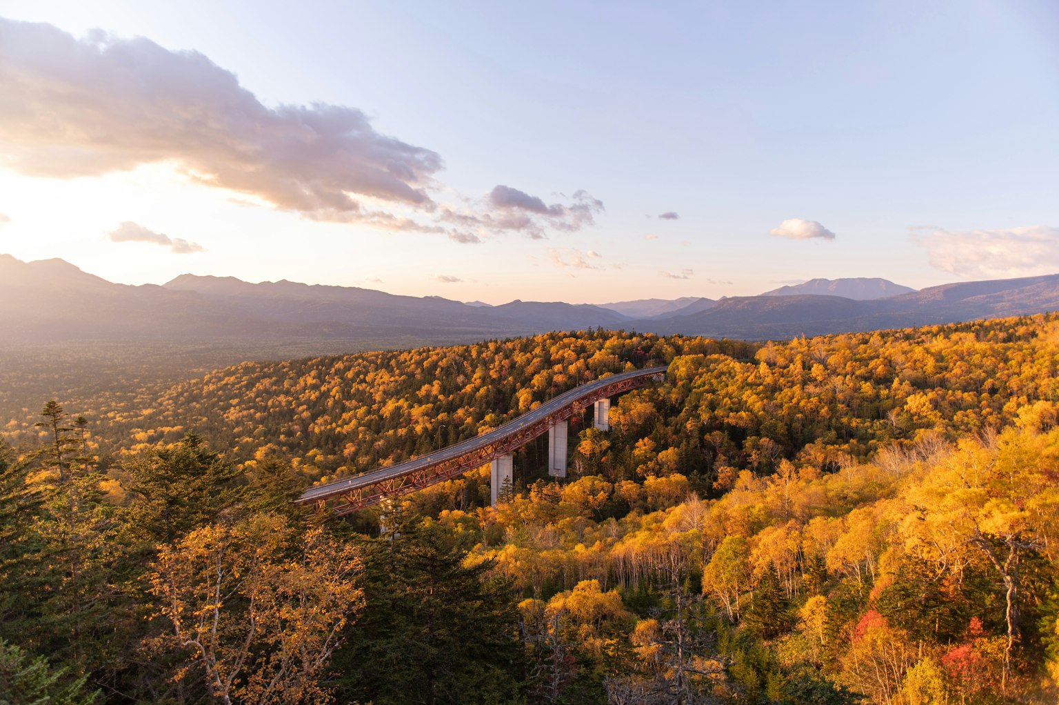 ทิวทัศน์ที่สวยงามของสะพานสูงล้อมรอบด้วยใบไม้ฤดูใบไม้ร่วงและภูเขา