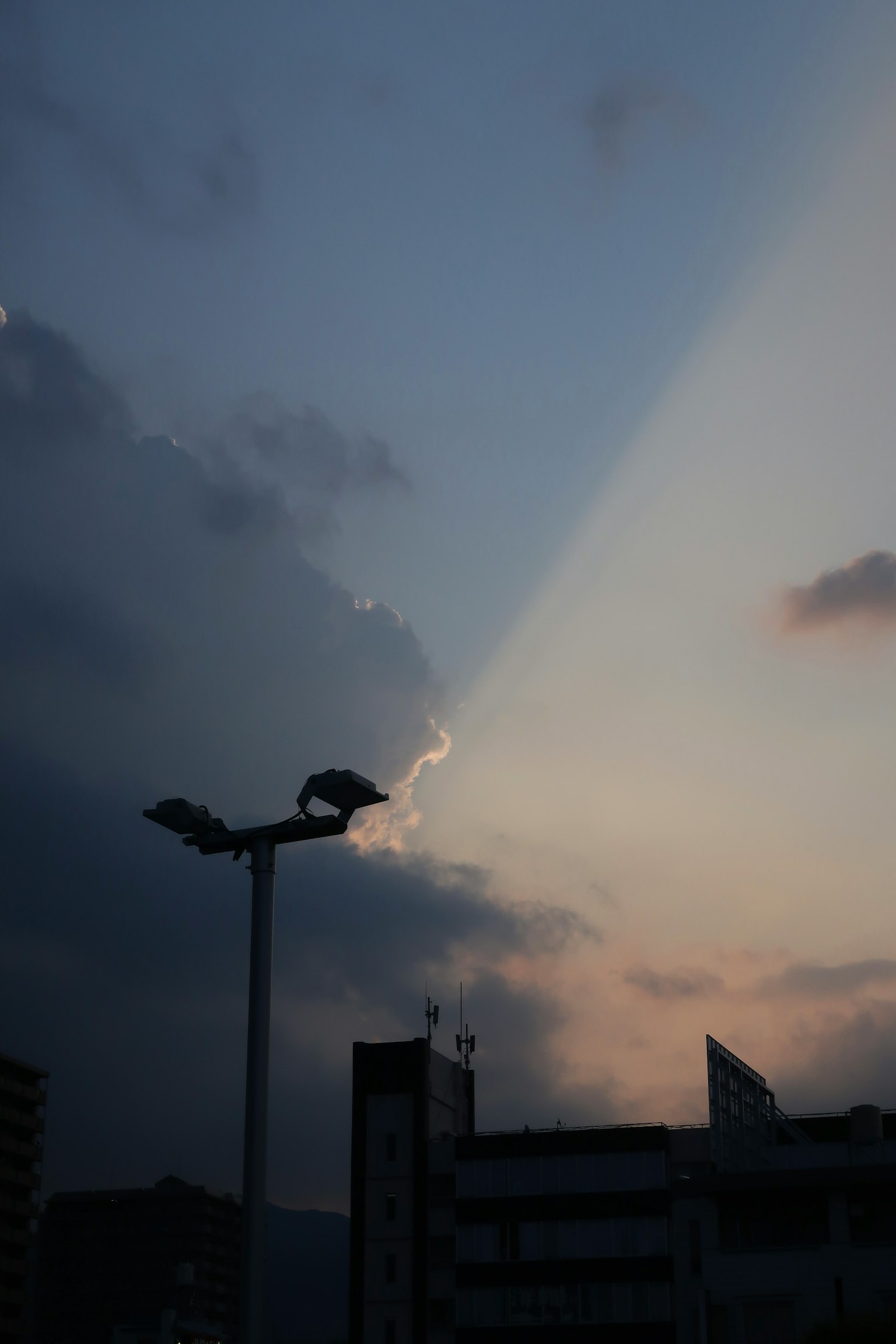 Tramonto drammatico con un fascio di luce che penetra tra le nuvole e un lampione