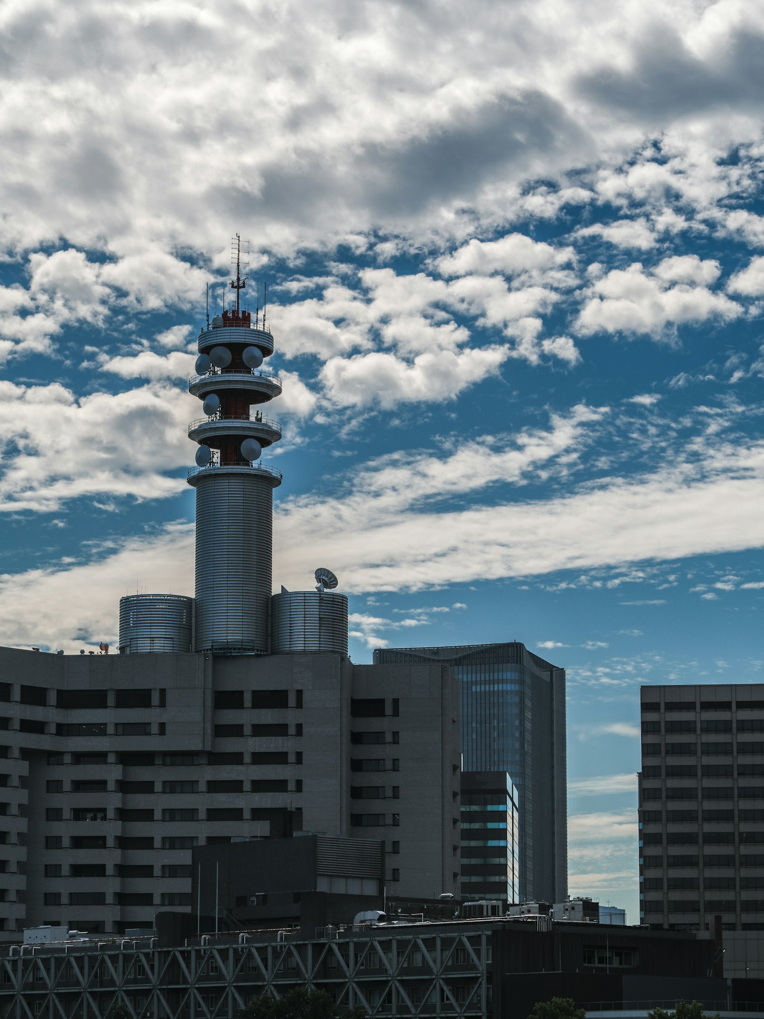 Menara komunikasi tinggi di latar belakang langit biru dan awan putih dengan bangunan modern