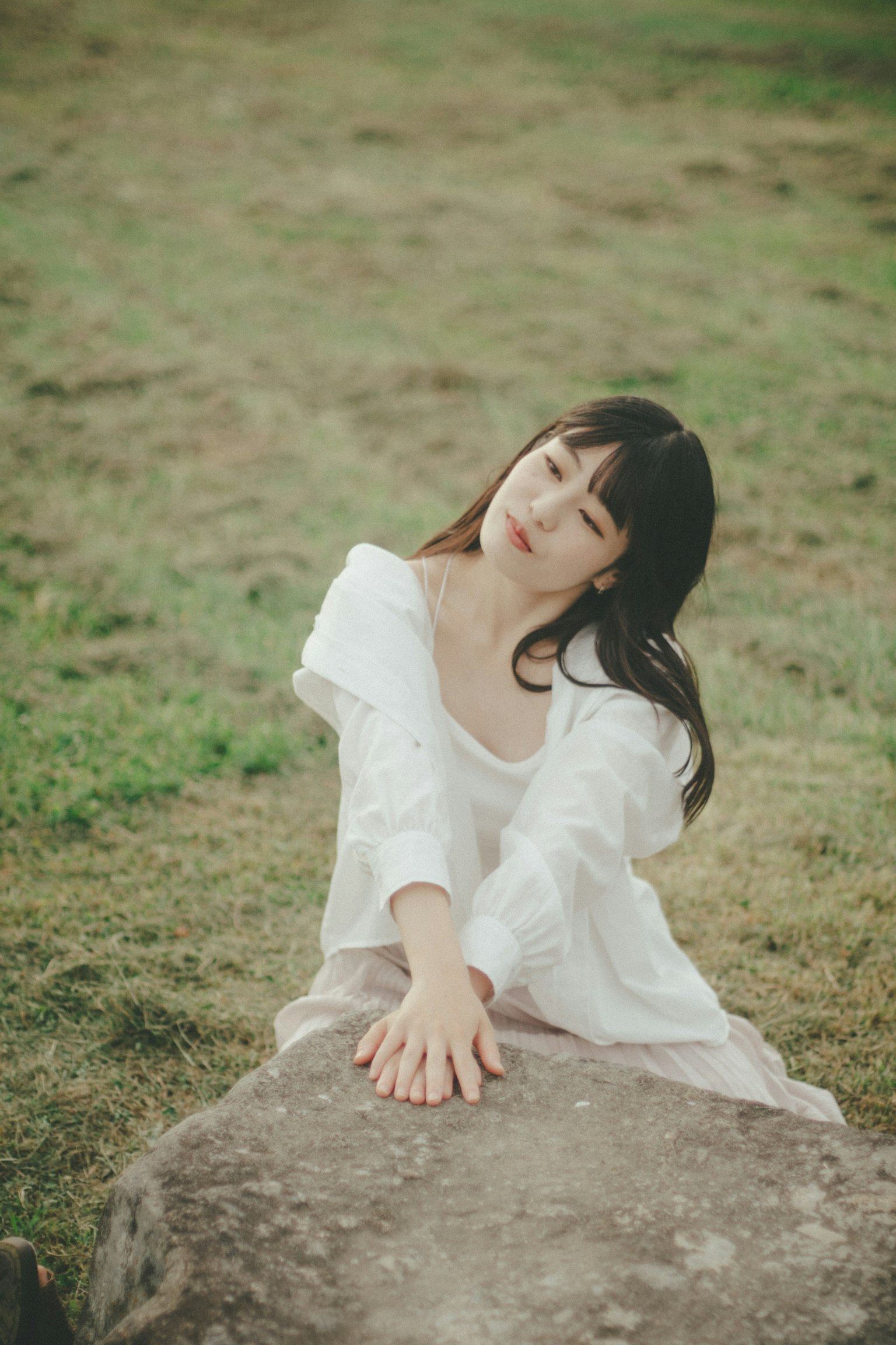 穿著白色裙子的女人坐在草地上的石頭上