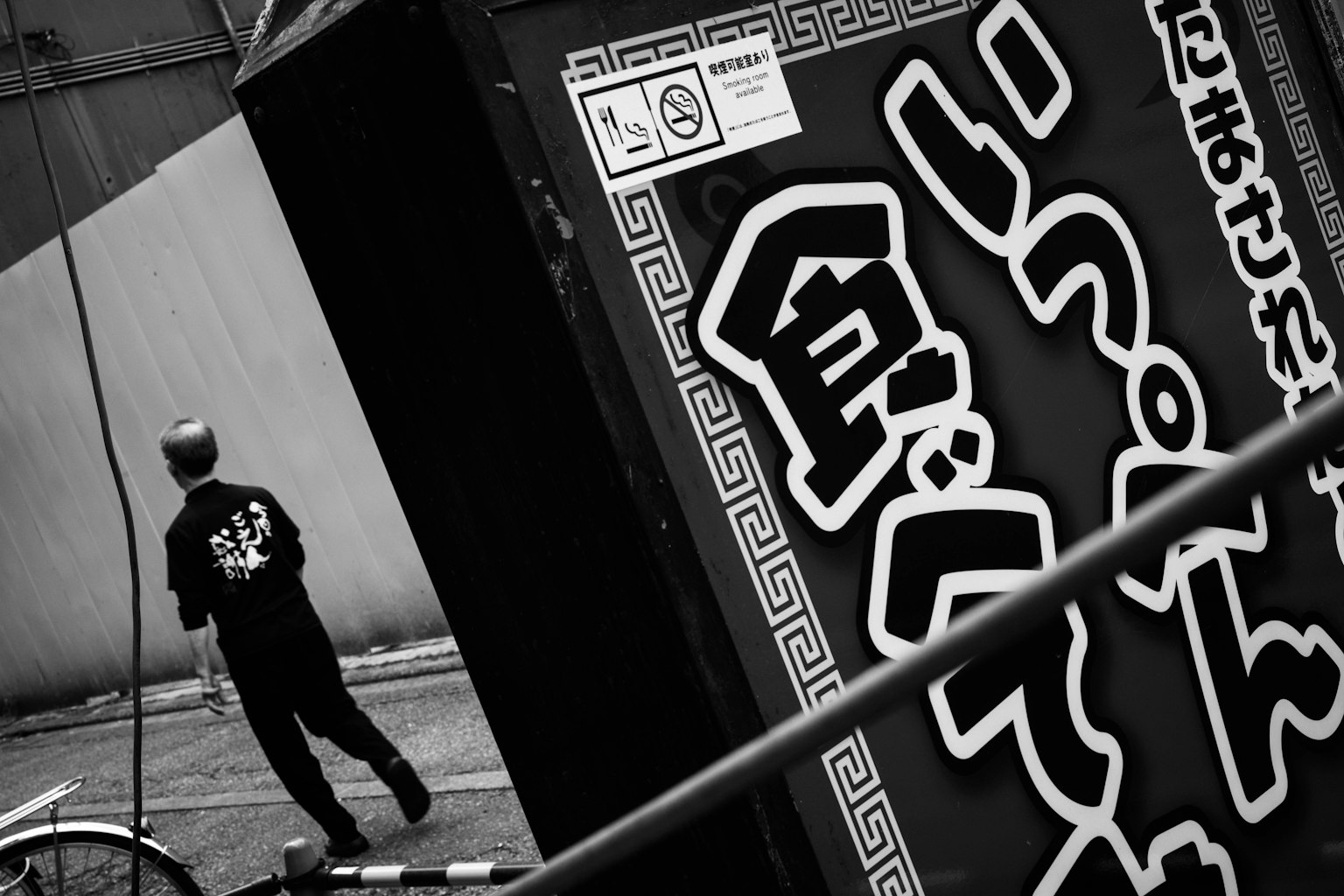 Un homme en chemise noire marchant devant un panneau en monochrome