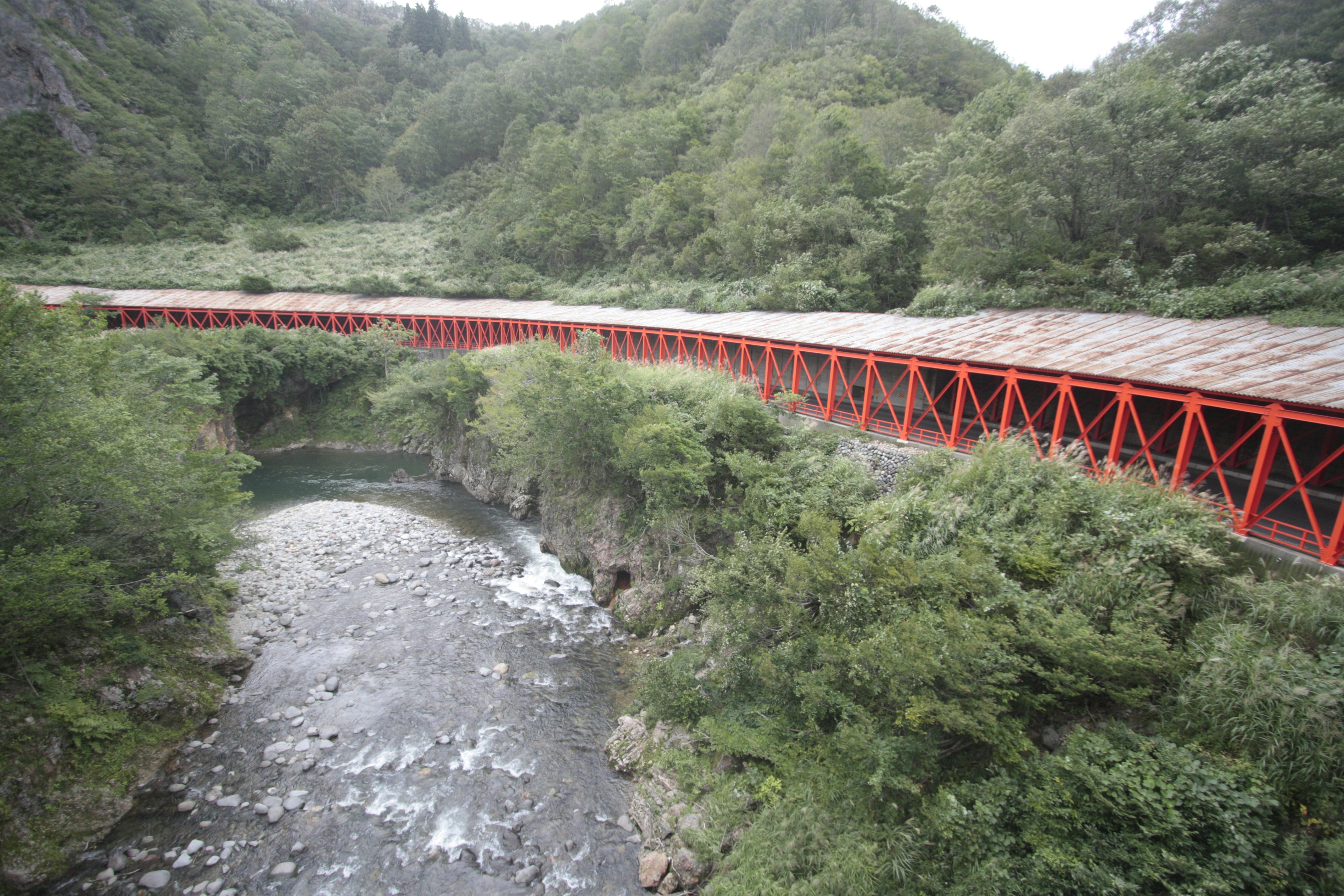 Red railway bridge crossing a green valley over a flowing river