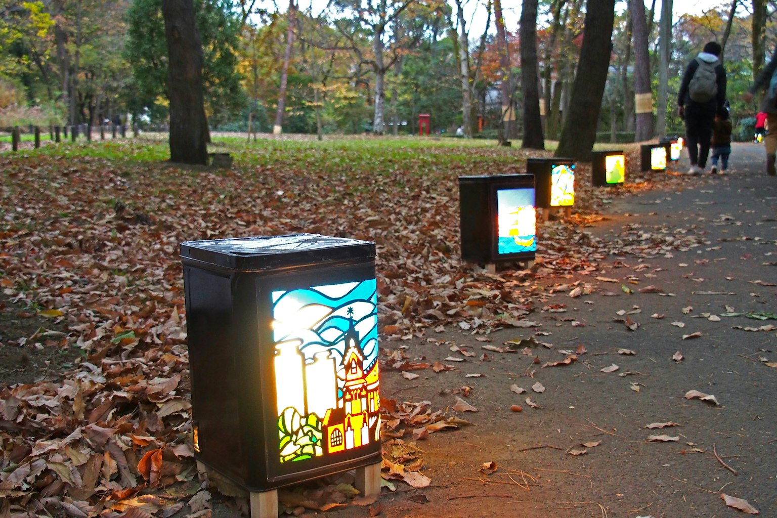Bunte Lampen entlang eines Weges in einem Herbstpark mit gefallenen Blättern