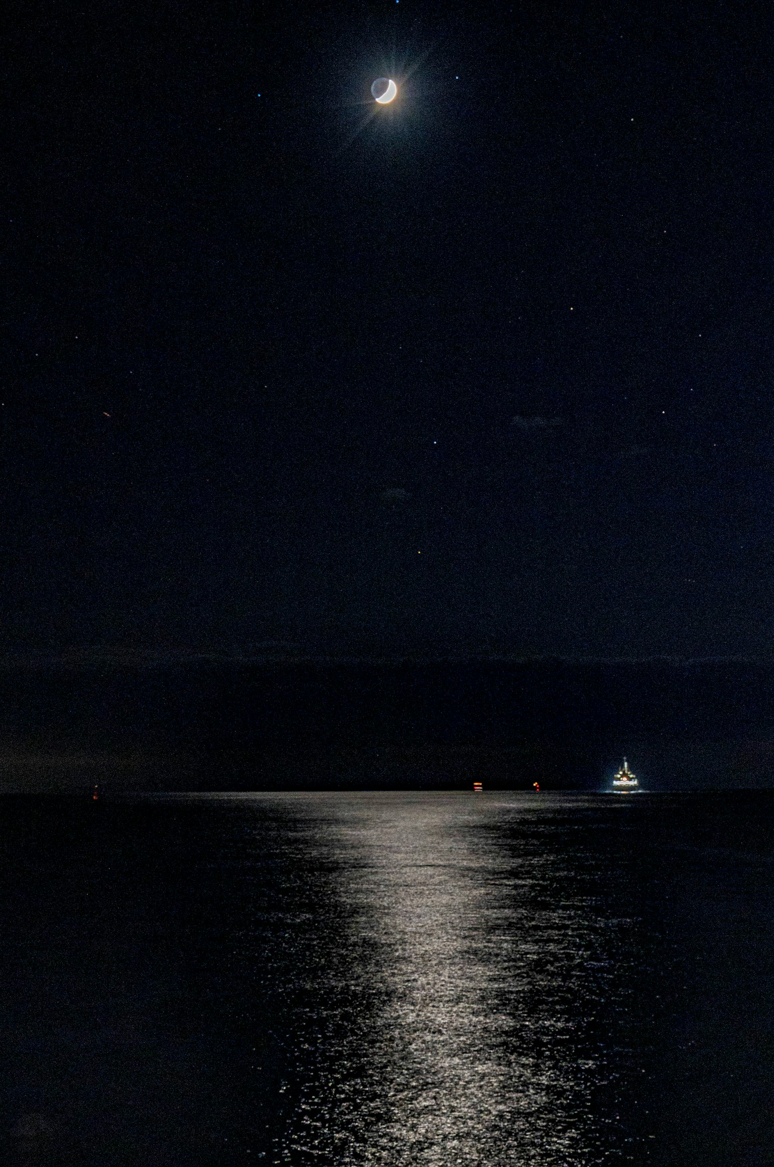 夜空中閃爍的月亮和星星，寧靜海面上的倒影，遠處的船