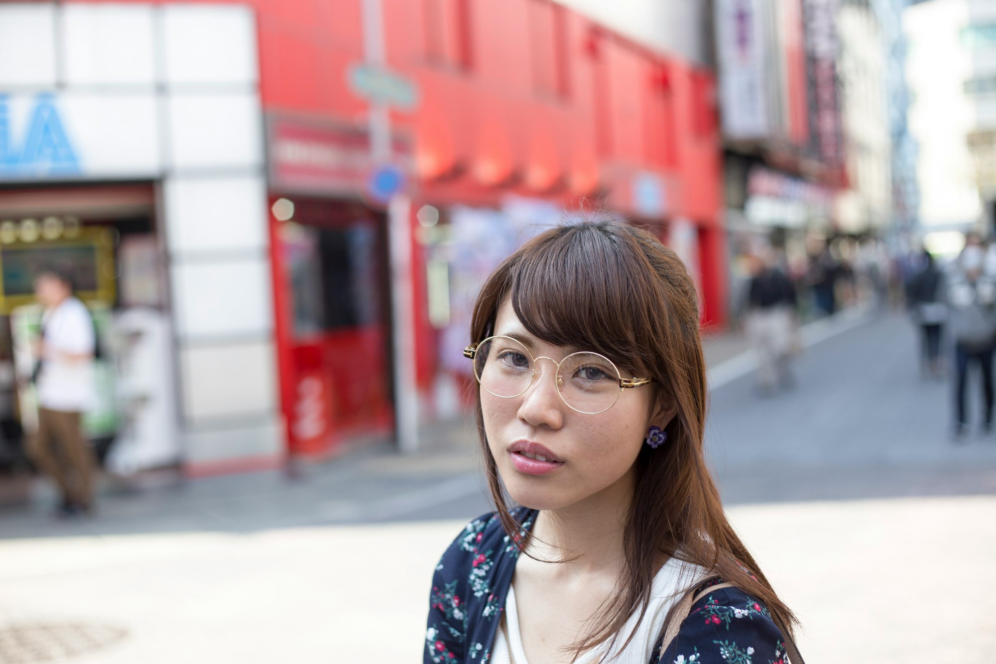 戴圓框眼鏡的女性回頭看，街道與紅色火車