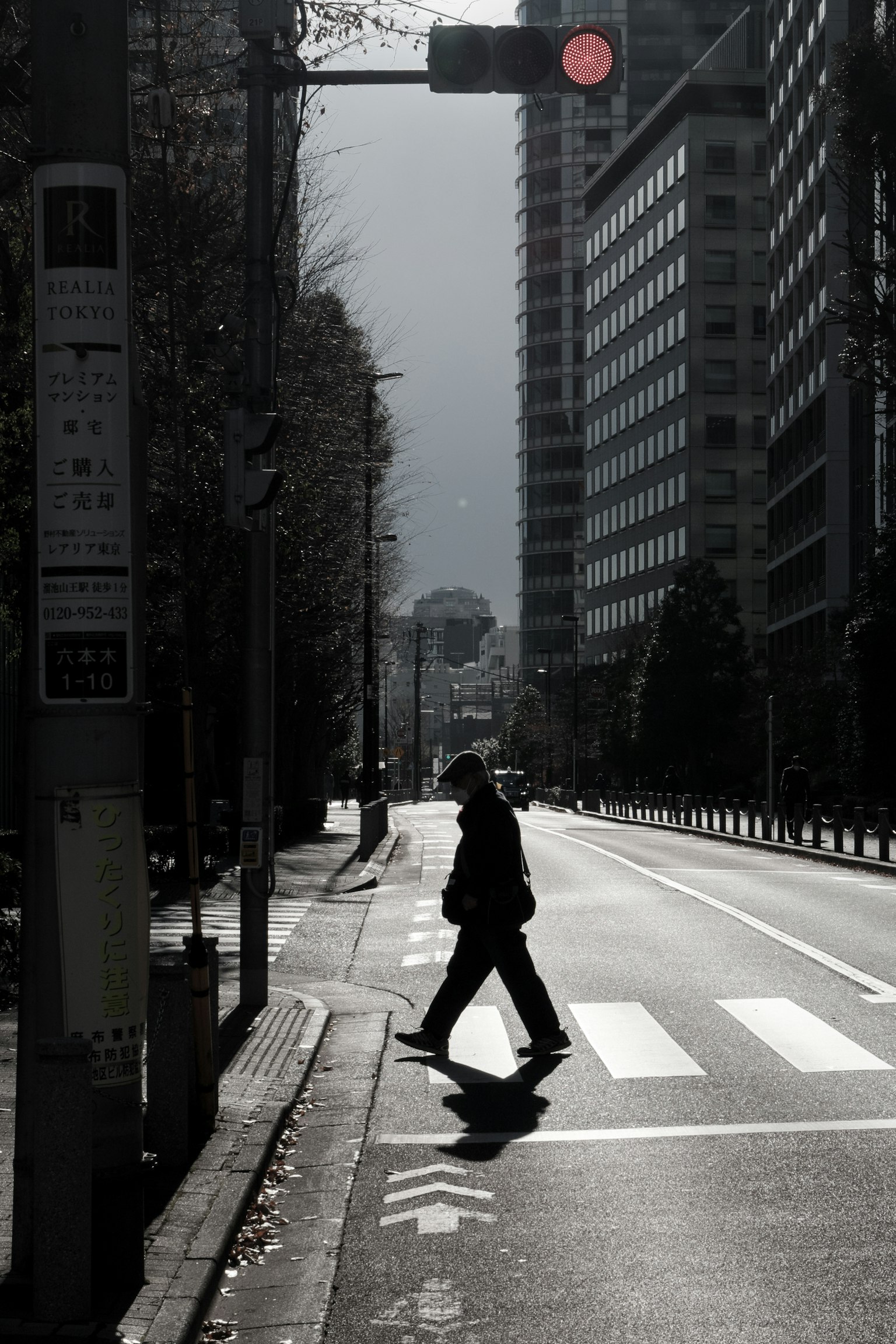 Silhouette of a person crossing a street at a crosswalk with a red traffic light