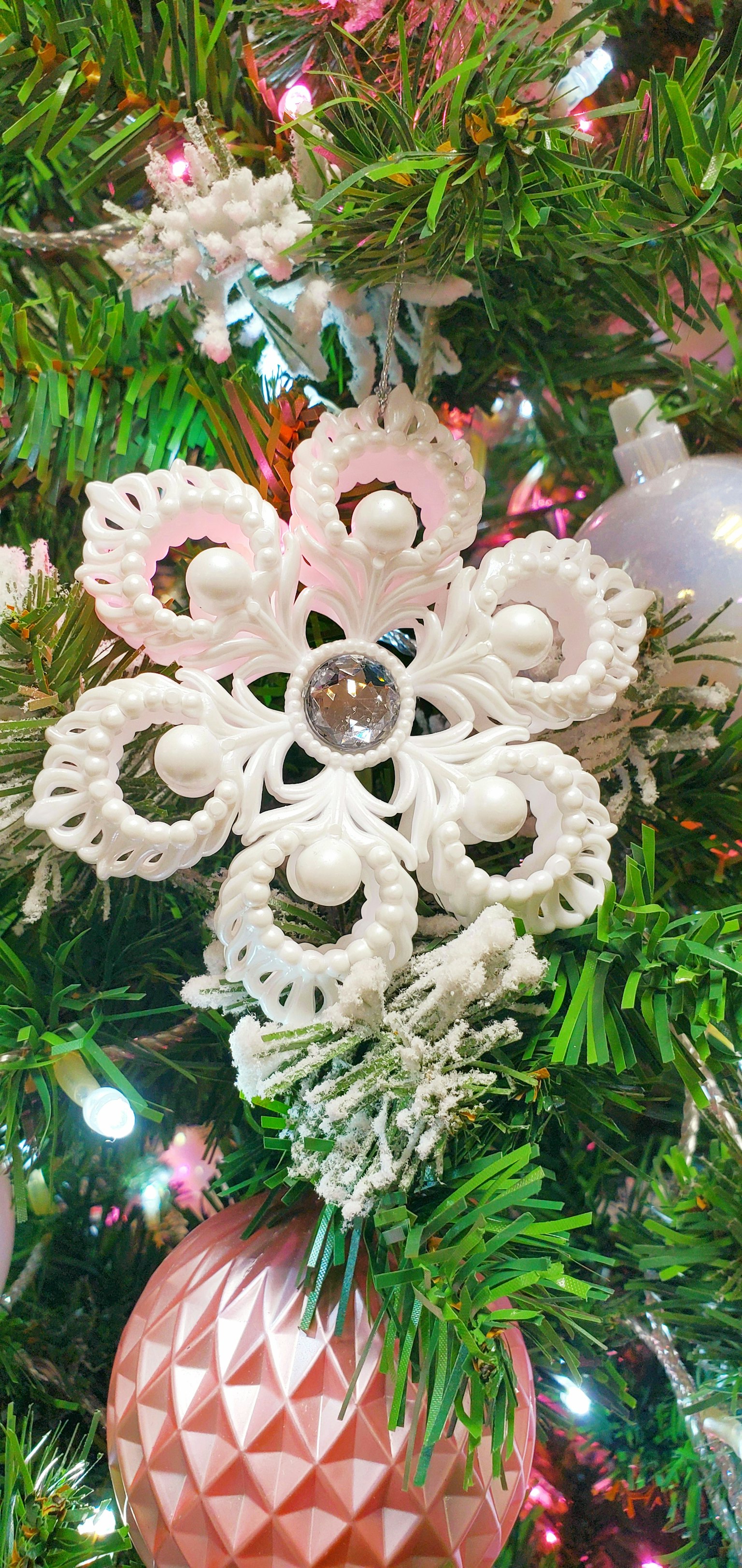 White snowflake ornament on a Christmas tree with pink decorations
