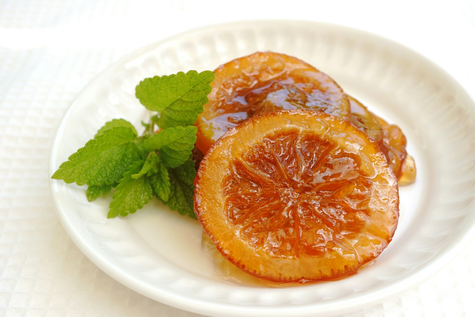 Fette d'arancia glassate su un piatto bianco con foglie di menta fresca