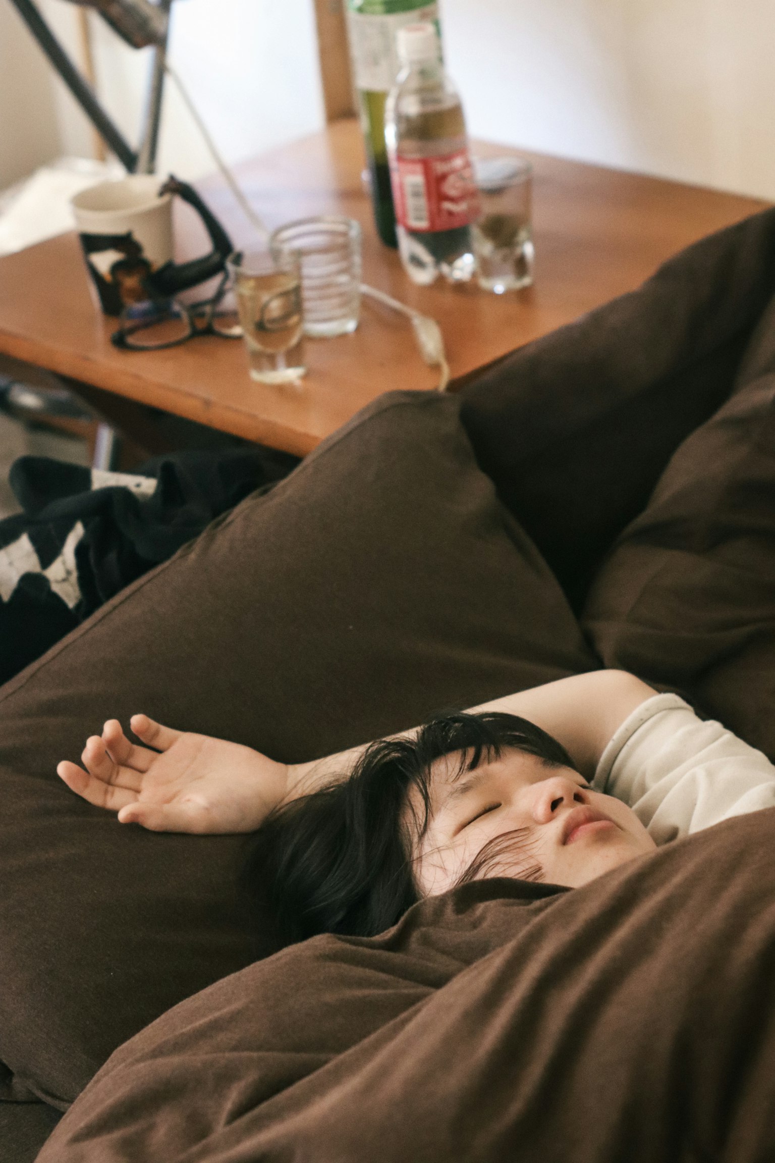 一名女性在床上睡觉，周围是棕色的靠垫和一张木桌
