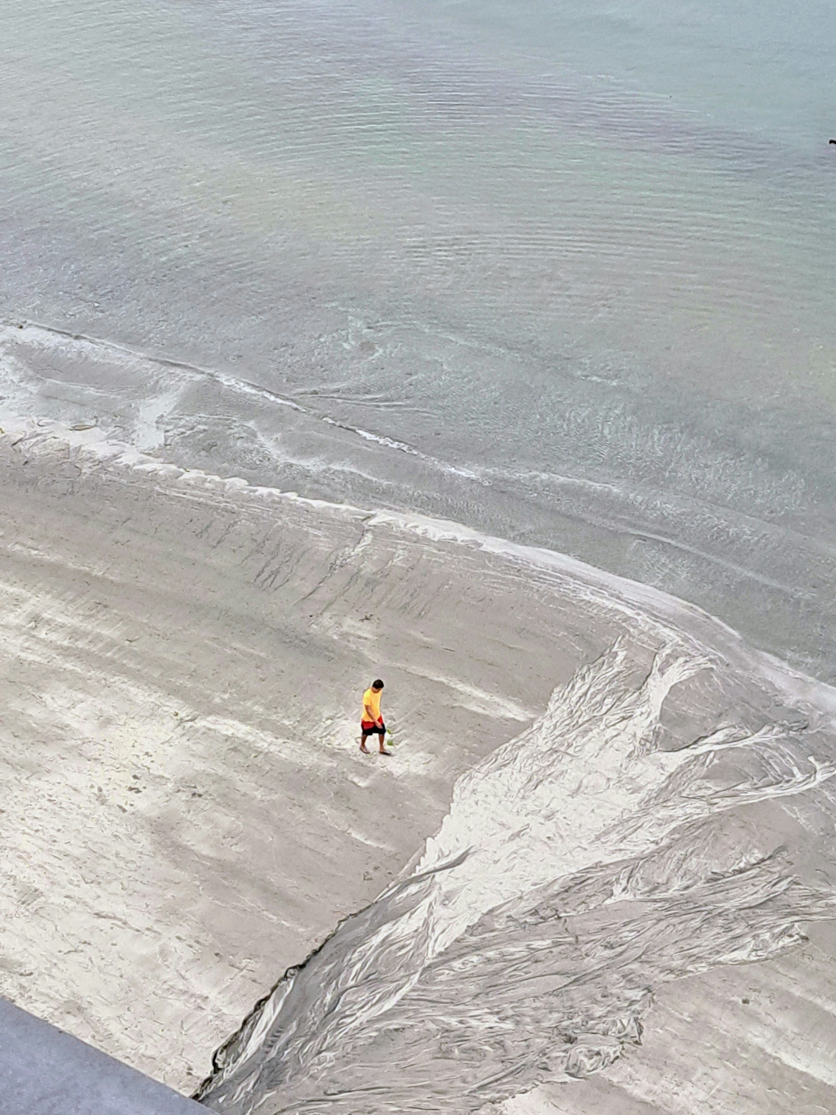 Küstenblick mit einer einzelnen Person, die über einen breiten Sandstrand geht