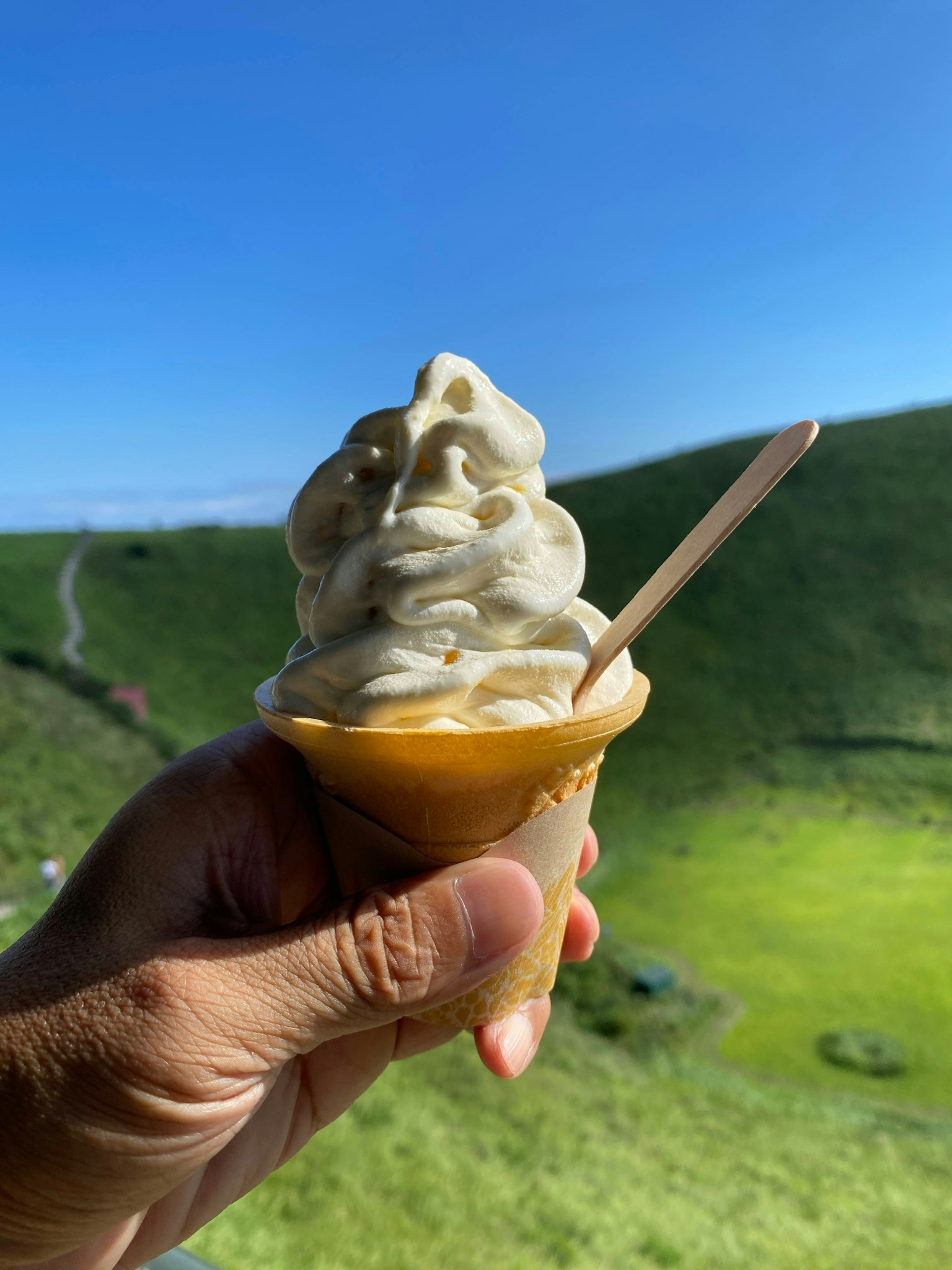 Tangan memegang kerucut es krim lembut dengan latar belakang bukit hijau
