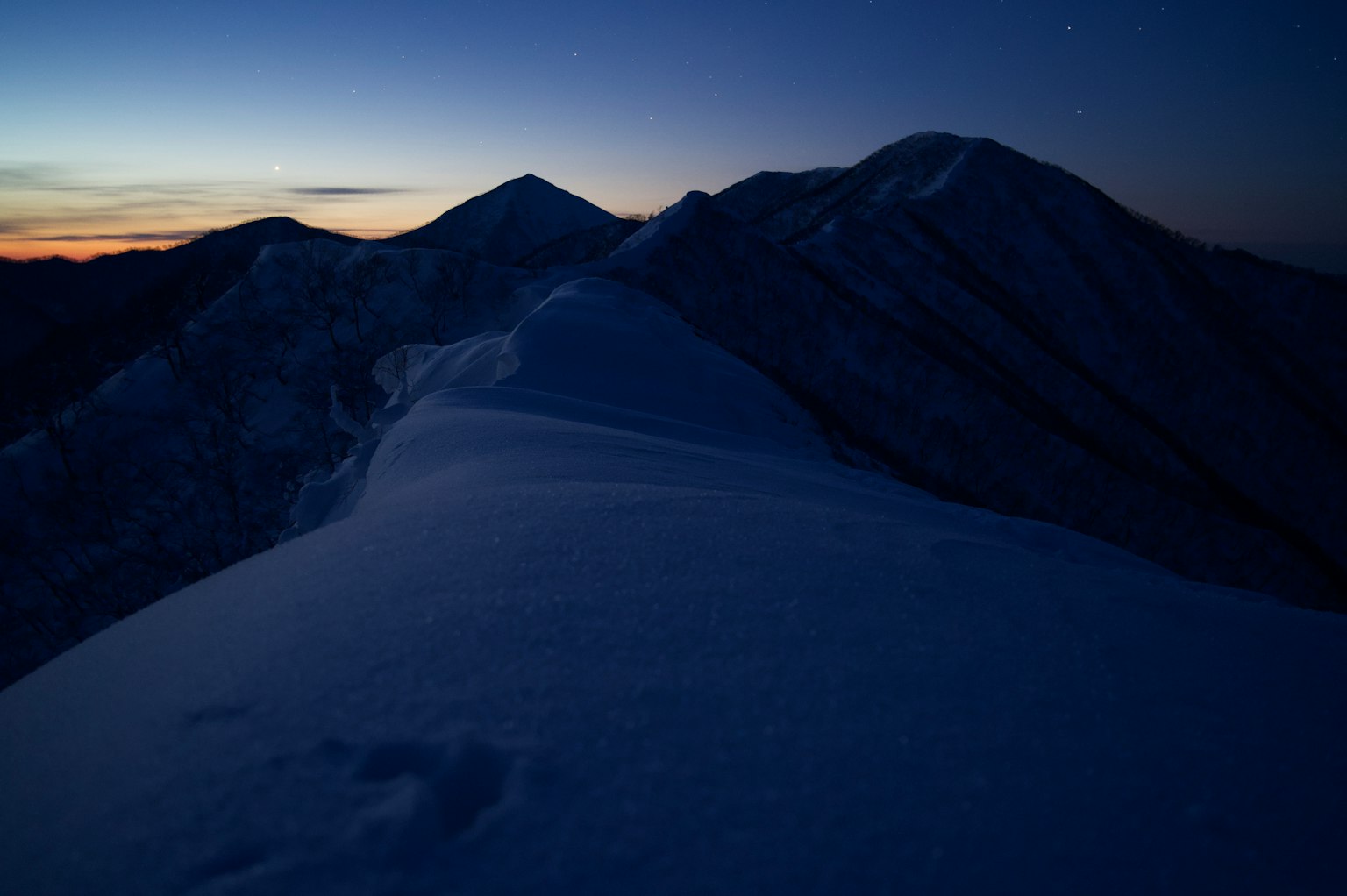 Snow-covered mountain peaks at dusk with twilight sky