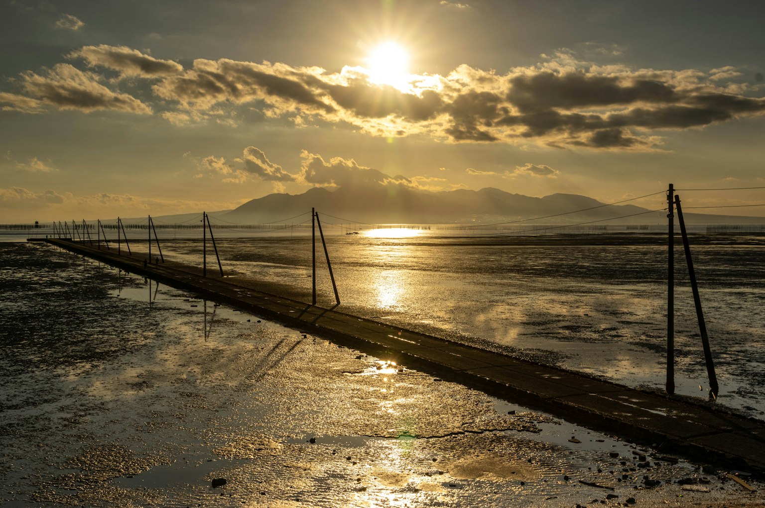 Scenic coastline at sunset with reflections on the water and silhouetted poles
