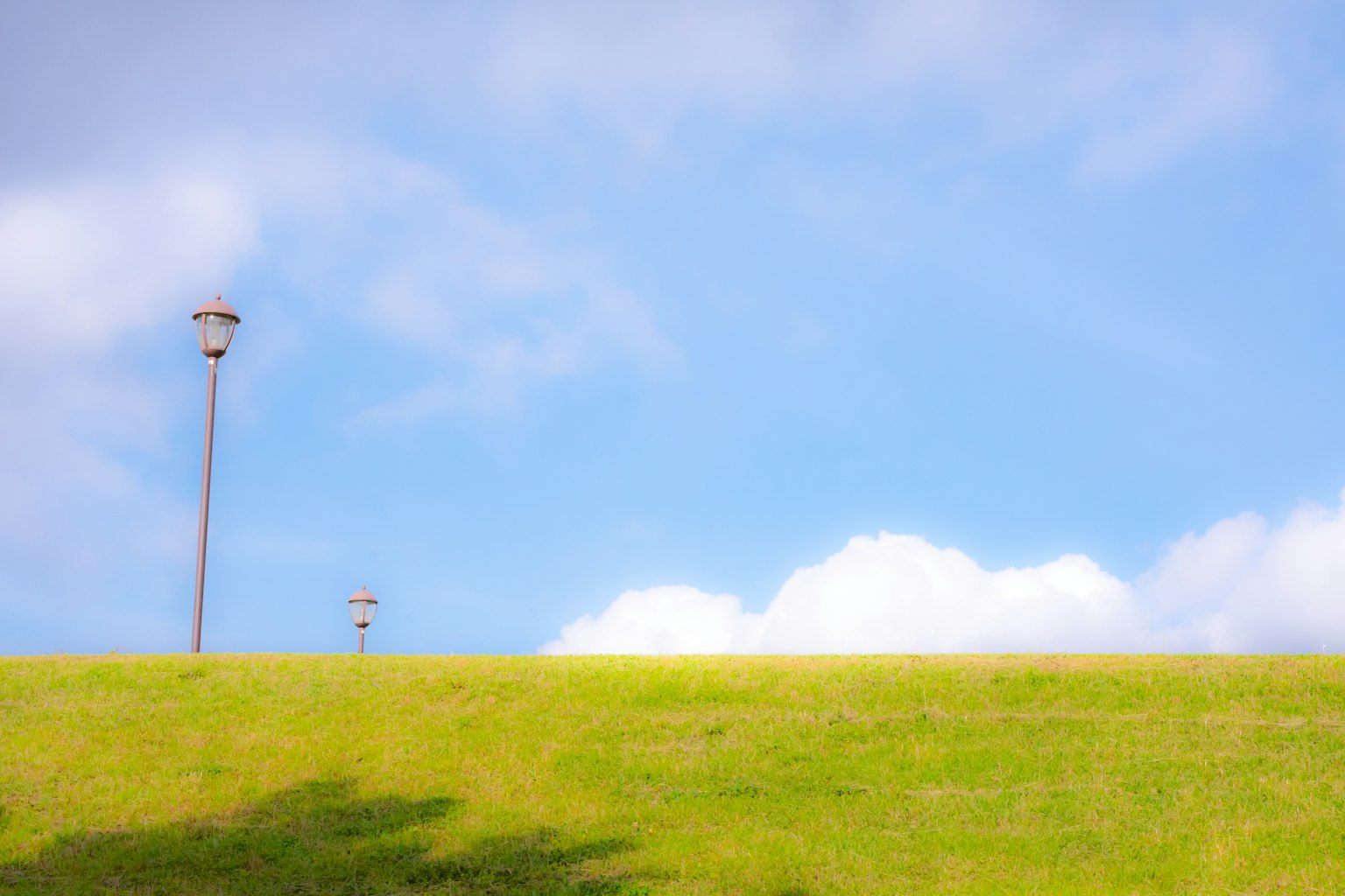 Colline verte sous un ciel bleu avec des nuages blancs et des lampadaires