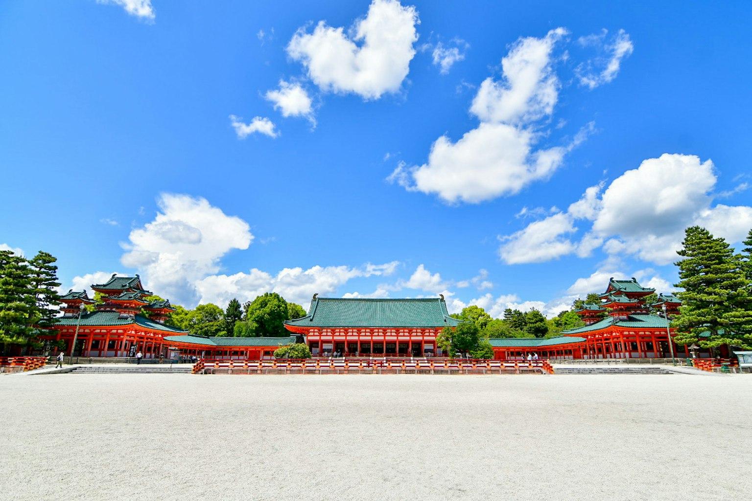 푸른 하늘과 흰 구름 아래 빨간 건물과 초록 나무가 있는 넓은 마당