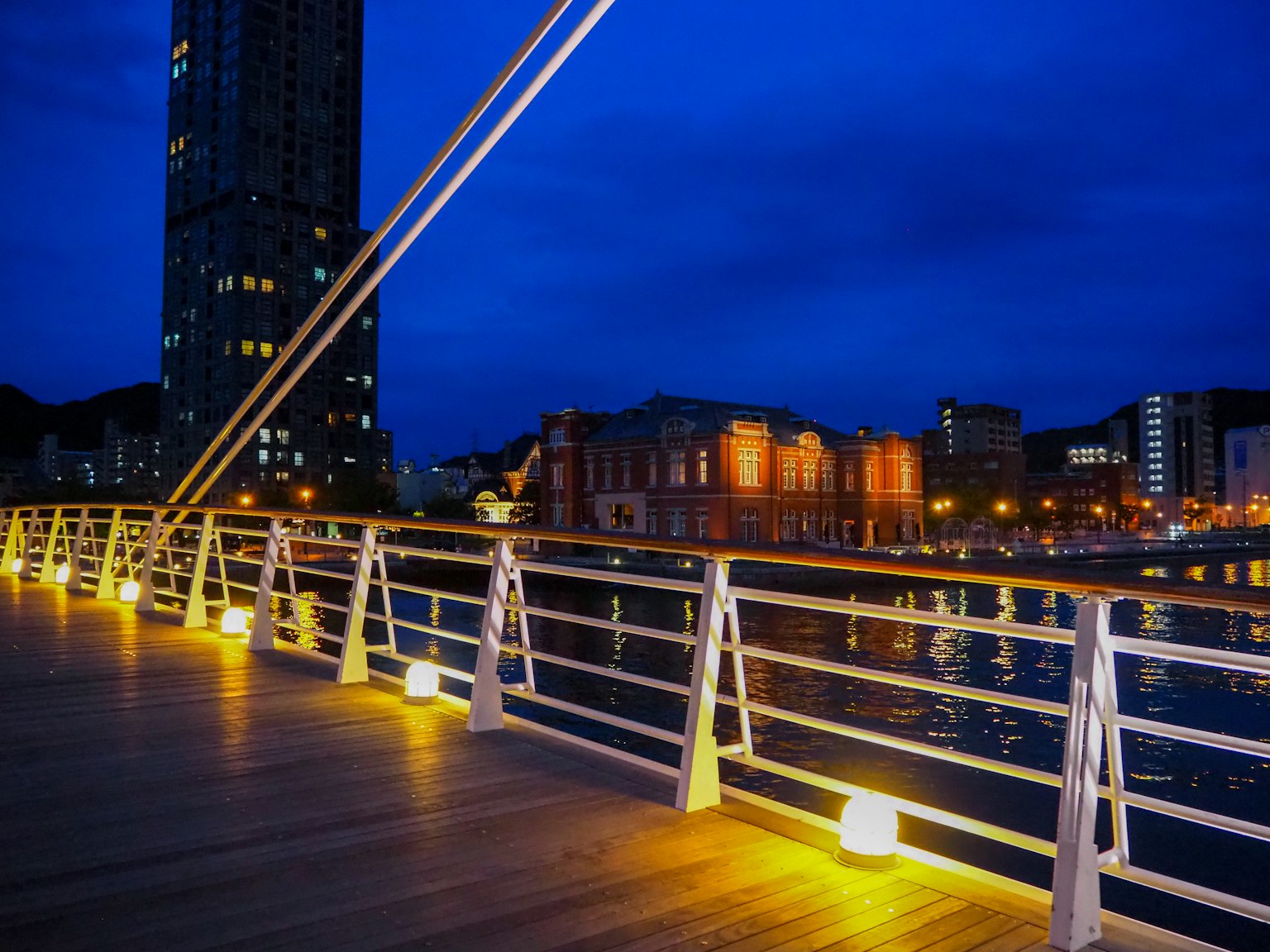 Vista escénica de un puente iluminado por la noche con luces de la ciudad reflejadas en el agua
