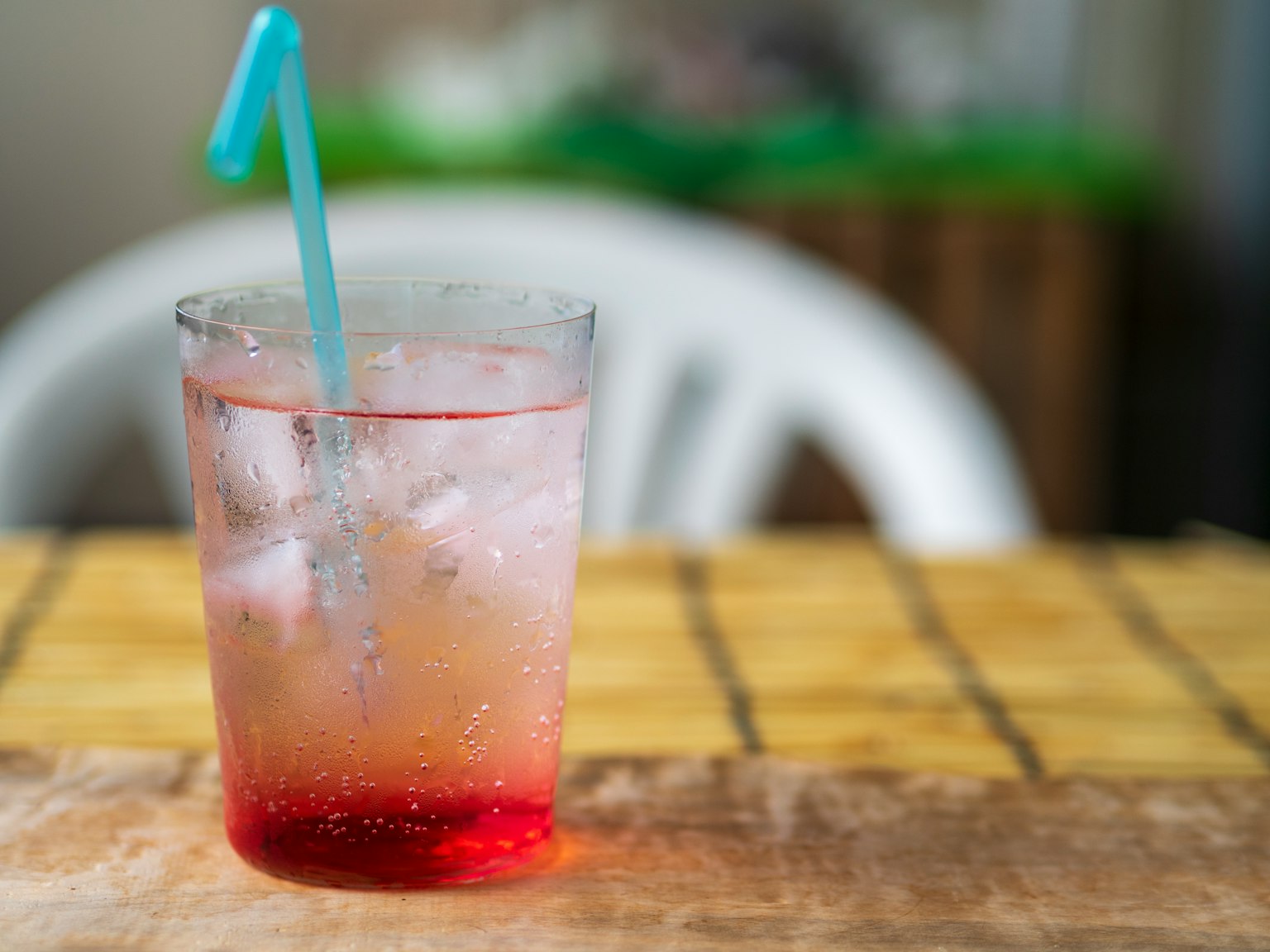 Gelas transparan dengan minuman merah dan es batu dengan sedotan biru