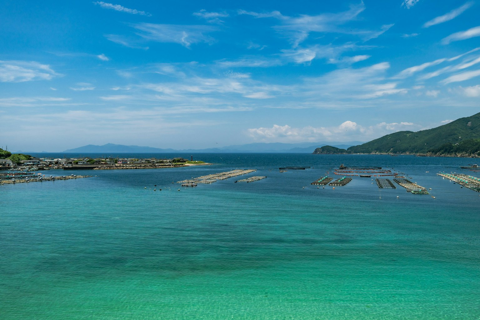 蓝色海洋和天空的风景 漂浮的水产养殖场 翠绿色的水面和山脉
