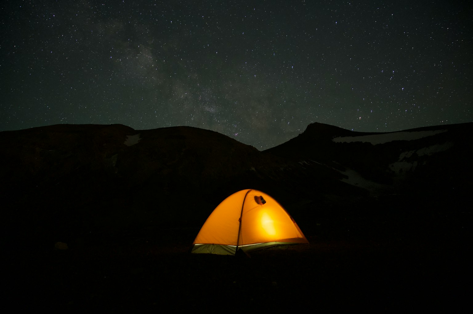 Tenda gialla sotto un cielo stellato con silhouette di montagna