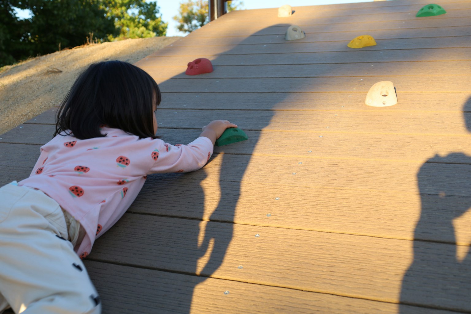 Kind, das an einer Kletterwand auf einem Spielplatz mit bunten Griffen klettert