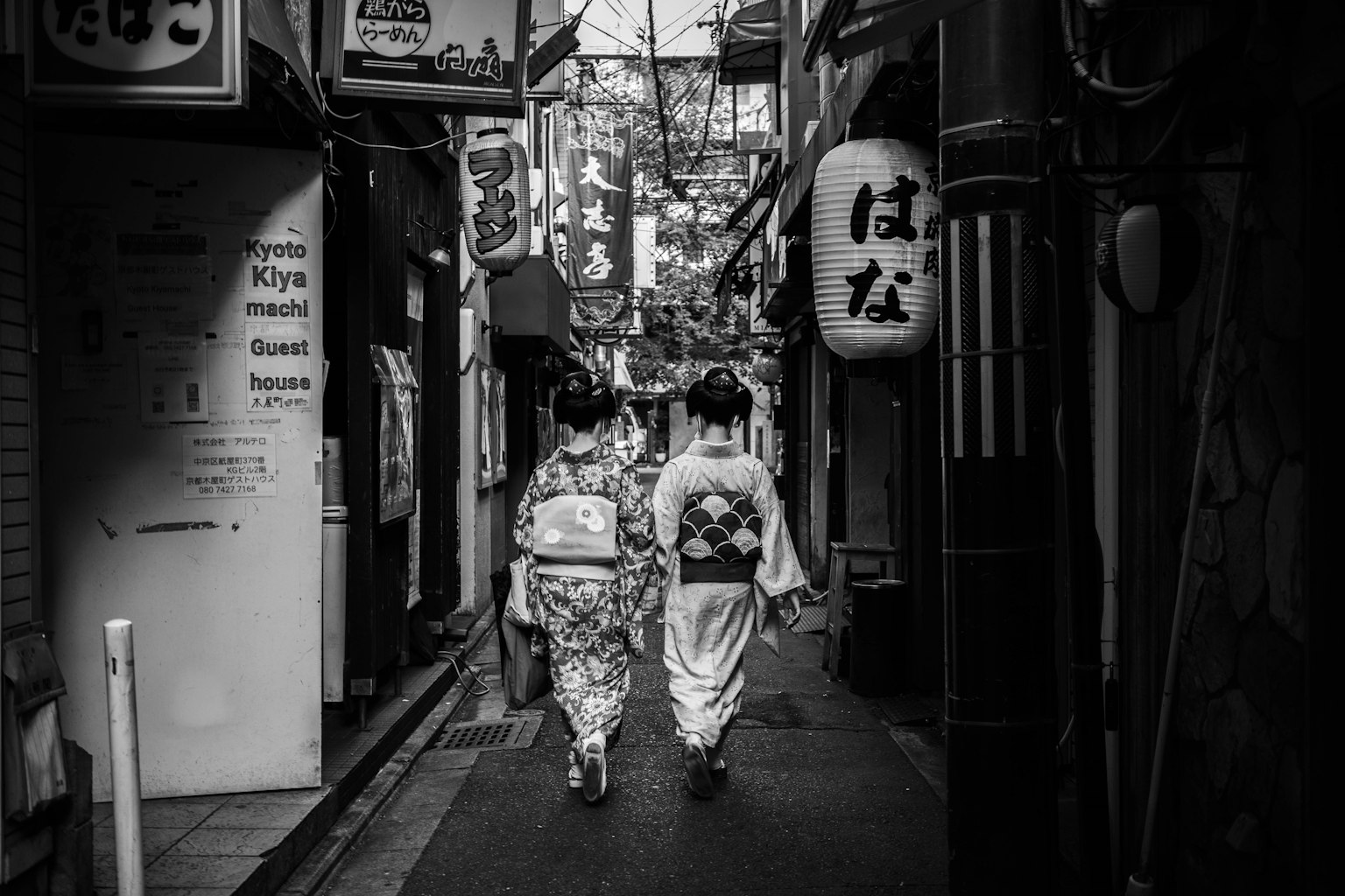 Dos mujeres en kimonos tradicionales caminando por un callejón estrecho en blanco y negro