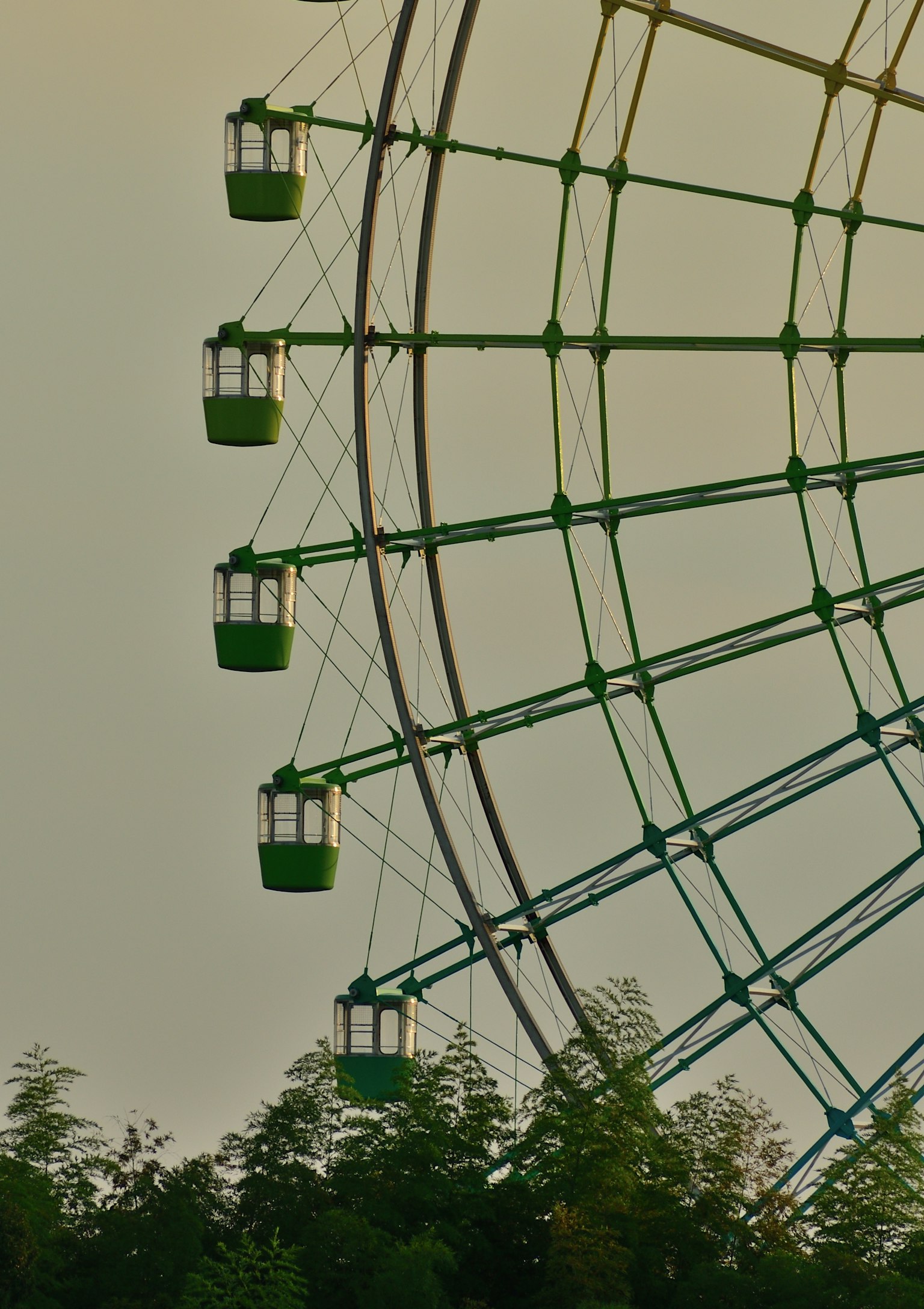 Green ferris wheel structure with passenger cabins
