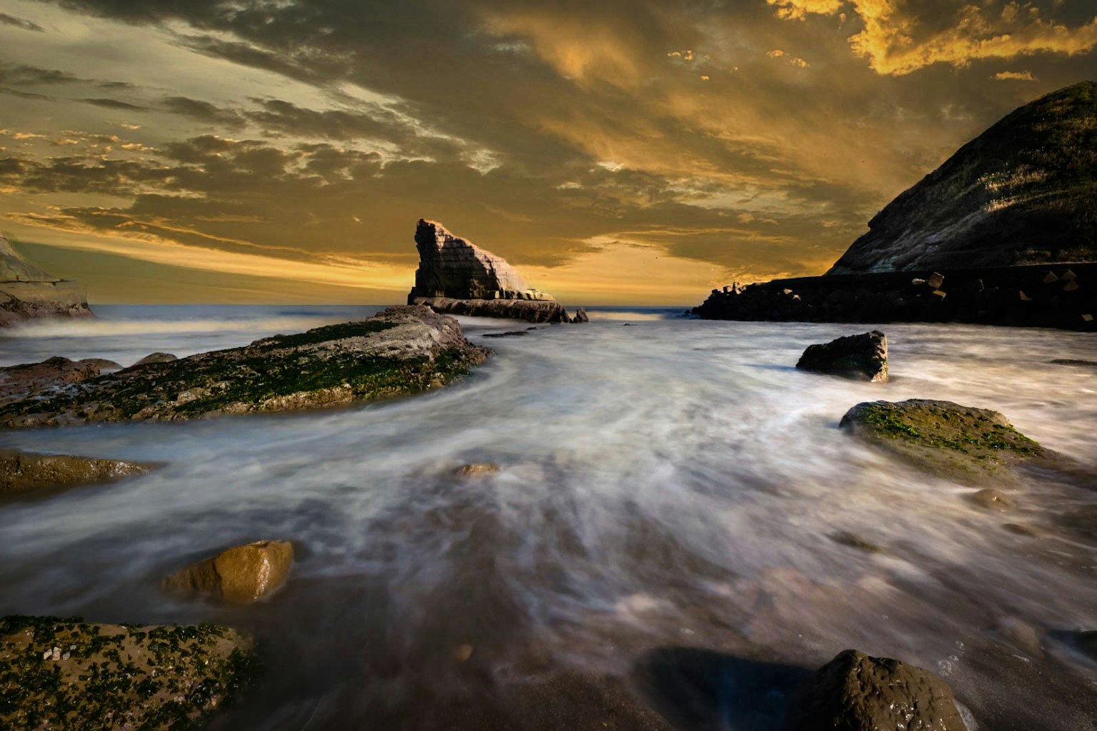 Paisaje costero con una formación rocosa y agua fluyendo al atardecer