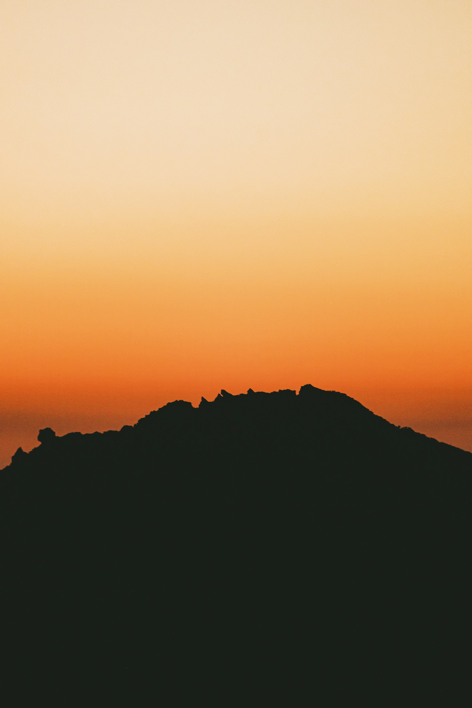 Silhouette of a mountain against an orange sunset sky