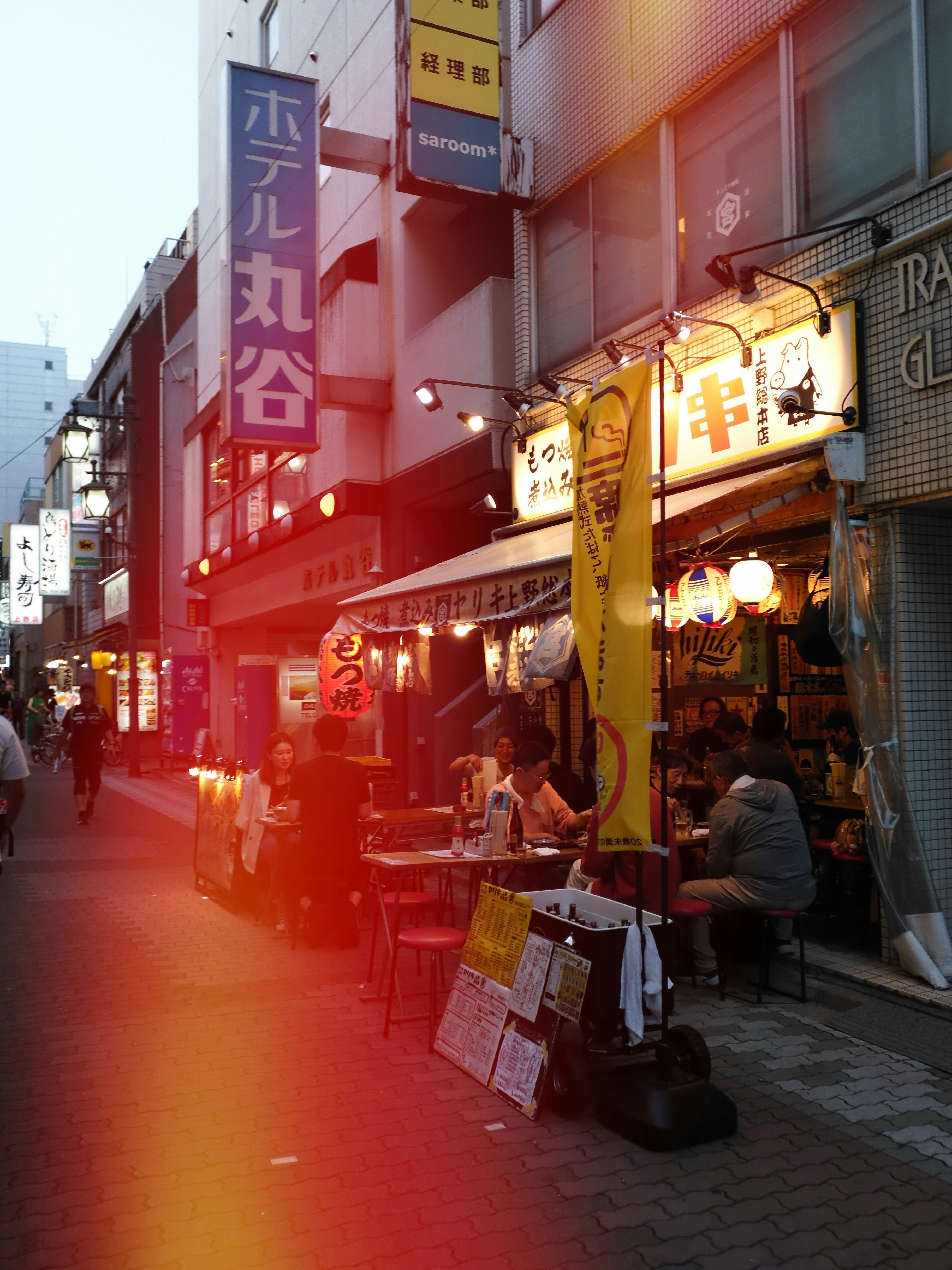 赤い外壁の飲食店が並ぶ路地の夕暮れの賑わい
